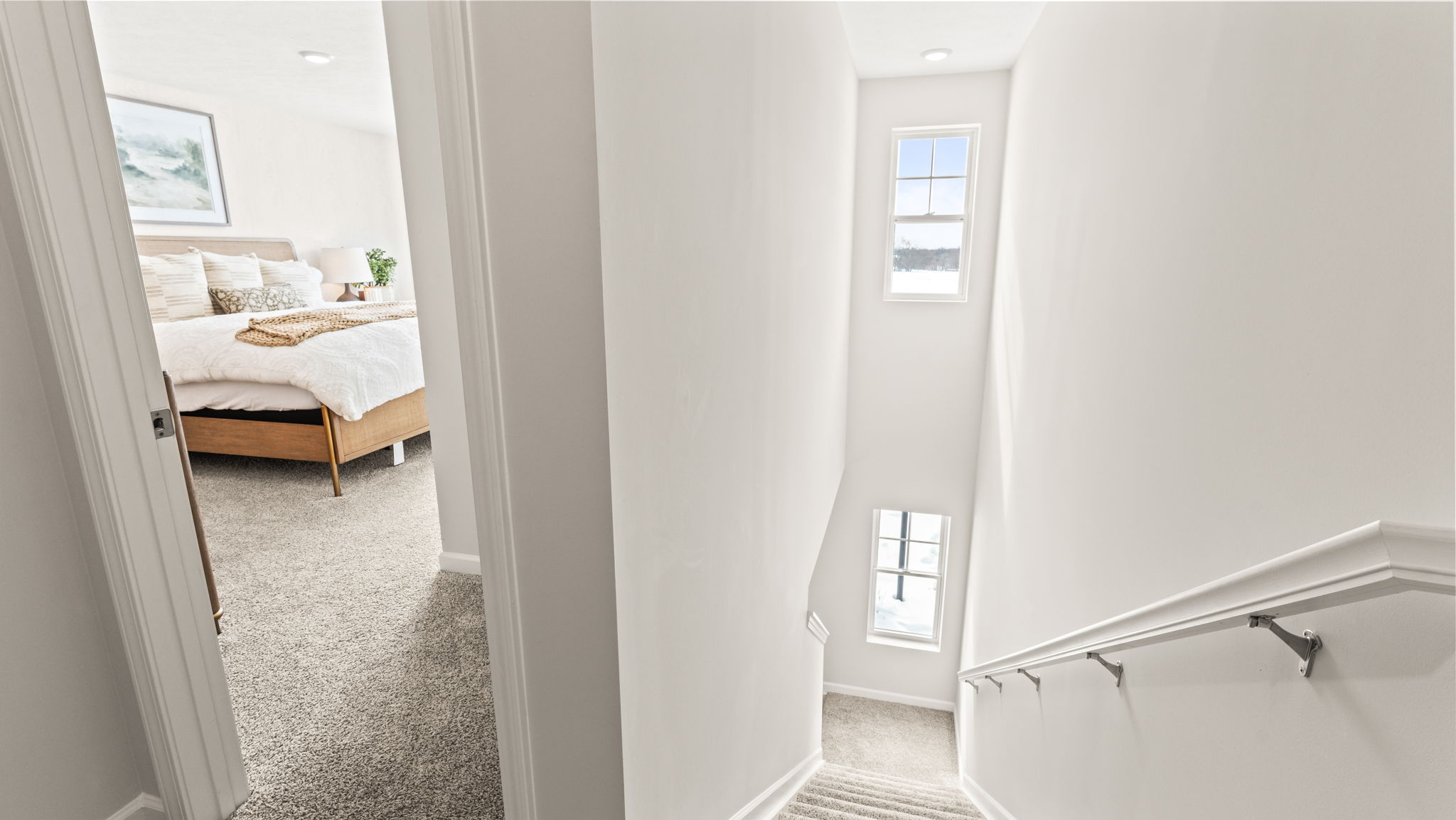 Upstairs landing with primary bedroom on the left and windows on the stairs letting in natural light on the right