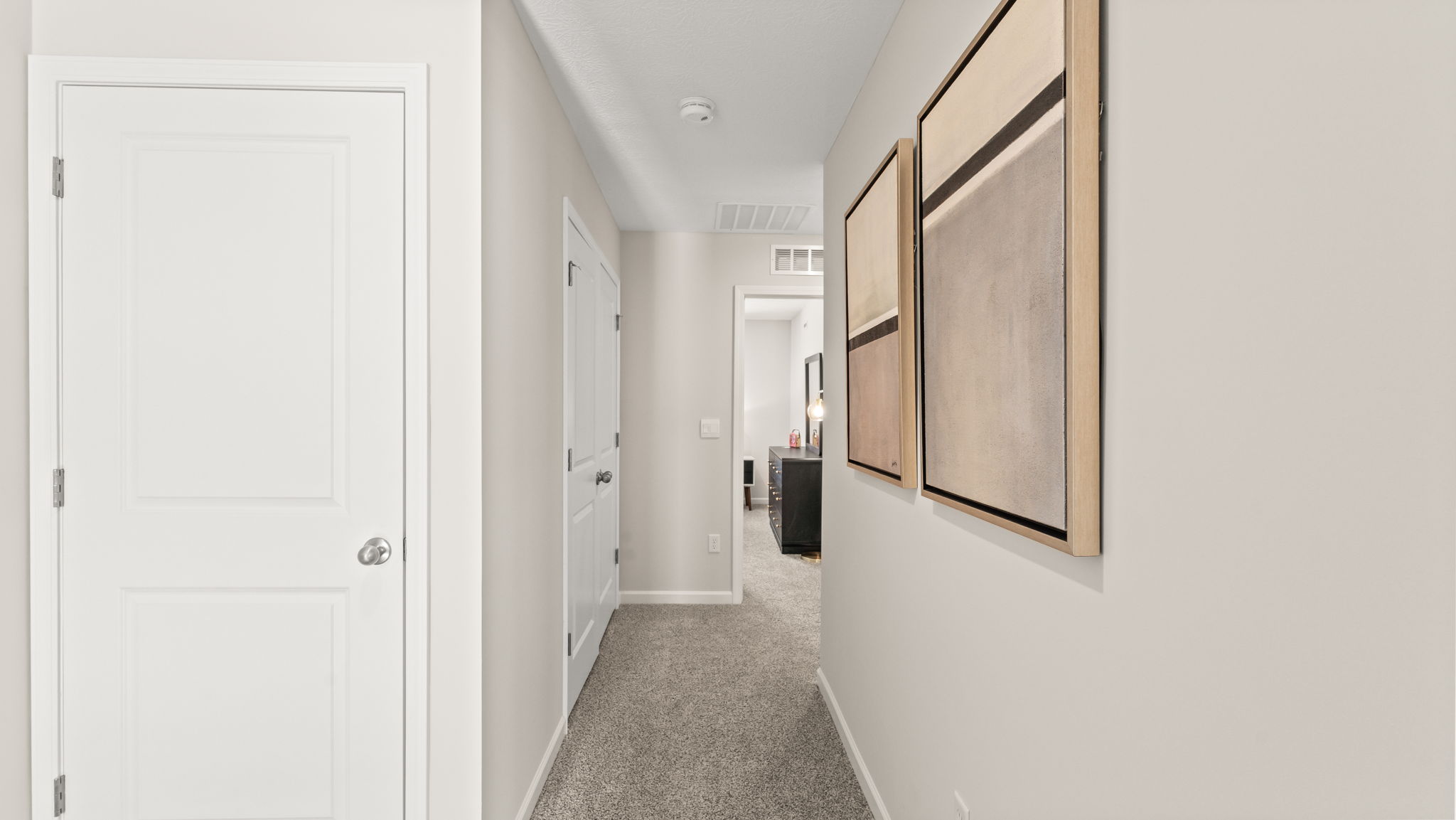 Second-level hallway with storage closet on the left of frame, passageway to bedrooms in the center, and modern art pieces on the wall with brown and grey earthy compositions