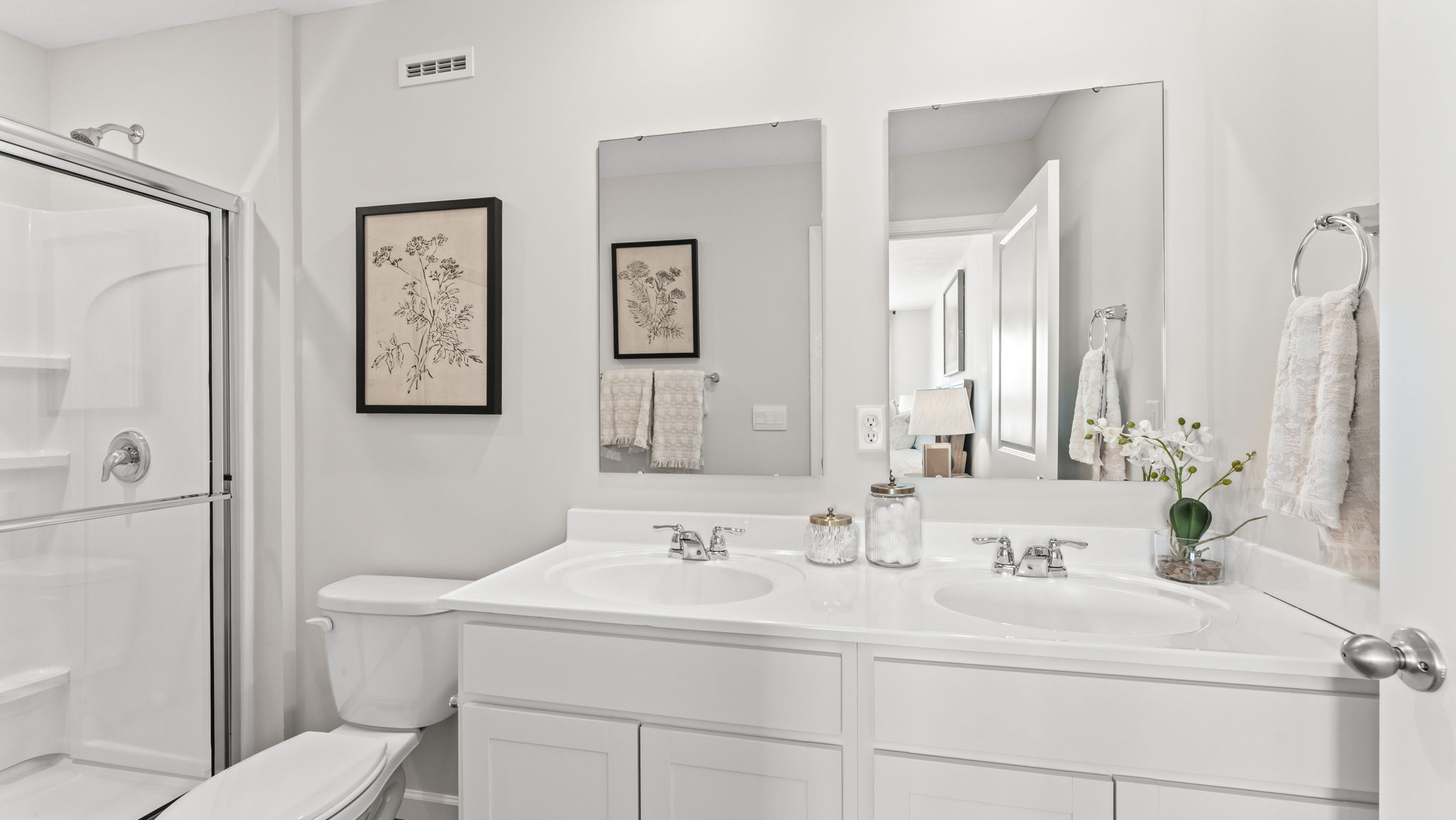 Primary bathroom suite with white cabinets and countertops, double bowl vanity, mirrors, and walk-in shower