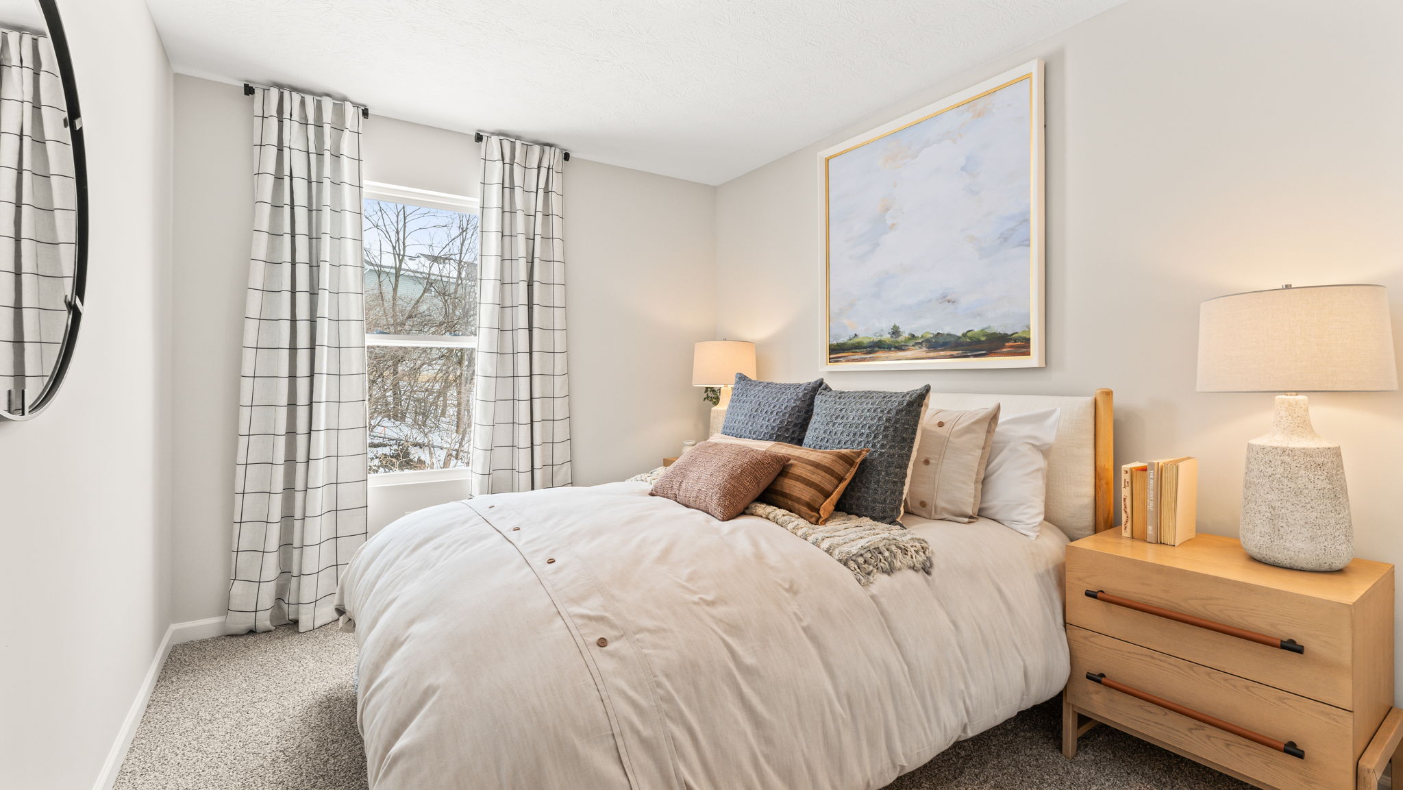 Three-quarter view of bedroom with lots of natural light, white comforter, oak nightstand, and artwork of a sky above the bed