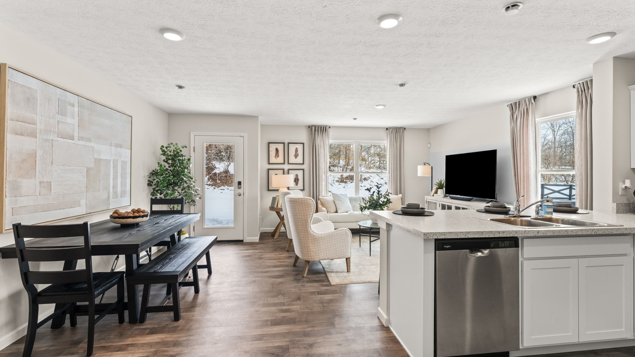 Full great area with abstract art on wall next to picnic style table, living room chairs and furniture, and kitchen on the right