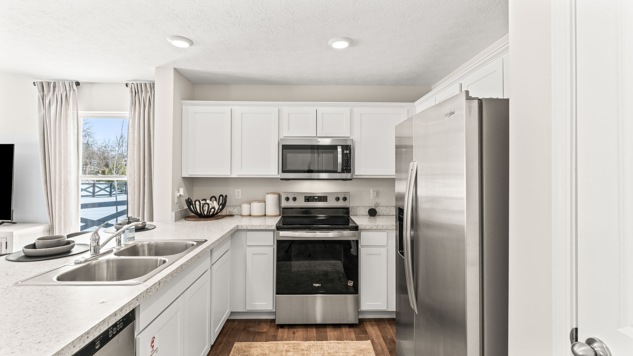 Side view of kitchen with tall white cabinetry, stainless steel appliances, and cultured marble kitchen countertops