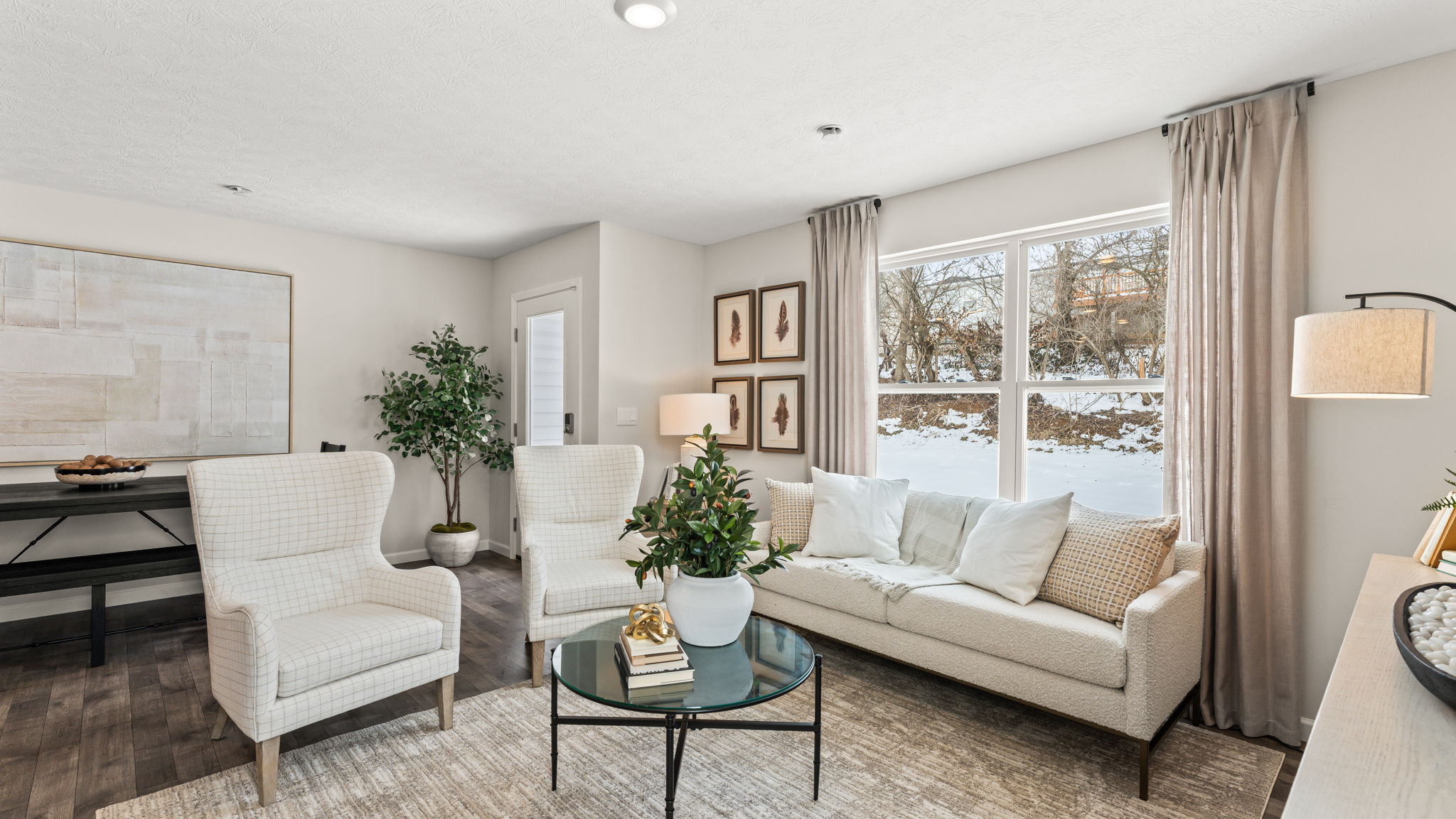 Modern cozy living room with soft white furniture accented by wood tones and a circular glass coffee table