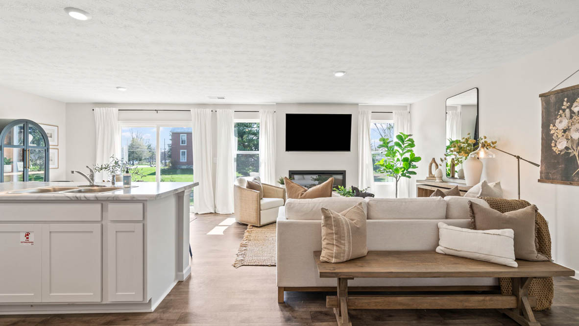 Full view of modern open-concept great room with comfy couches, elegant dining area, and white cabinets on kitchen island.