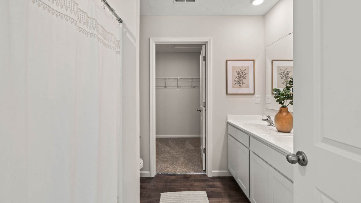 shotgun view of primary bathroom with sinks and walkin closet.