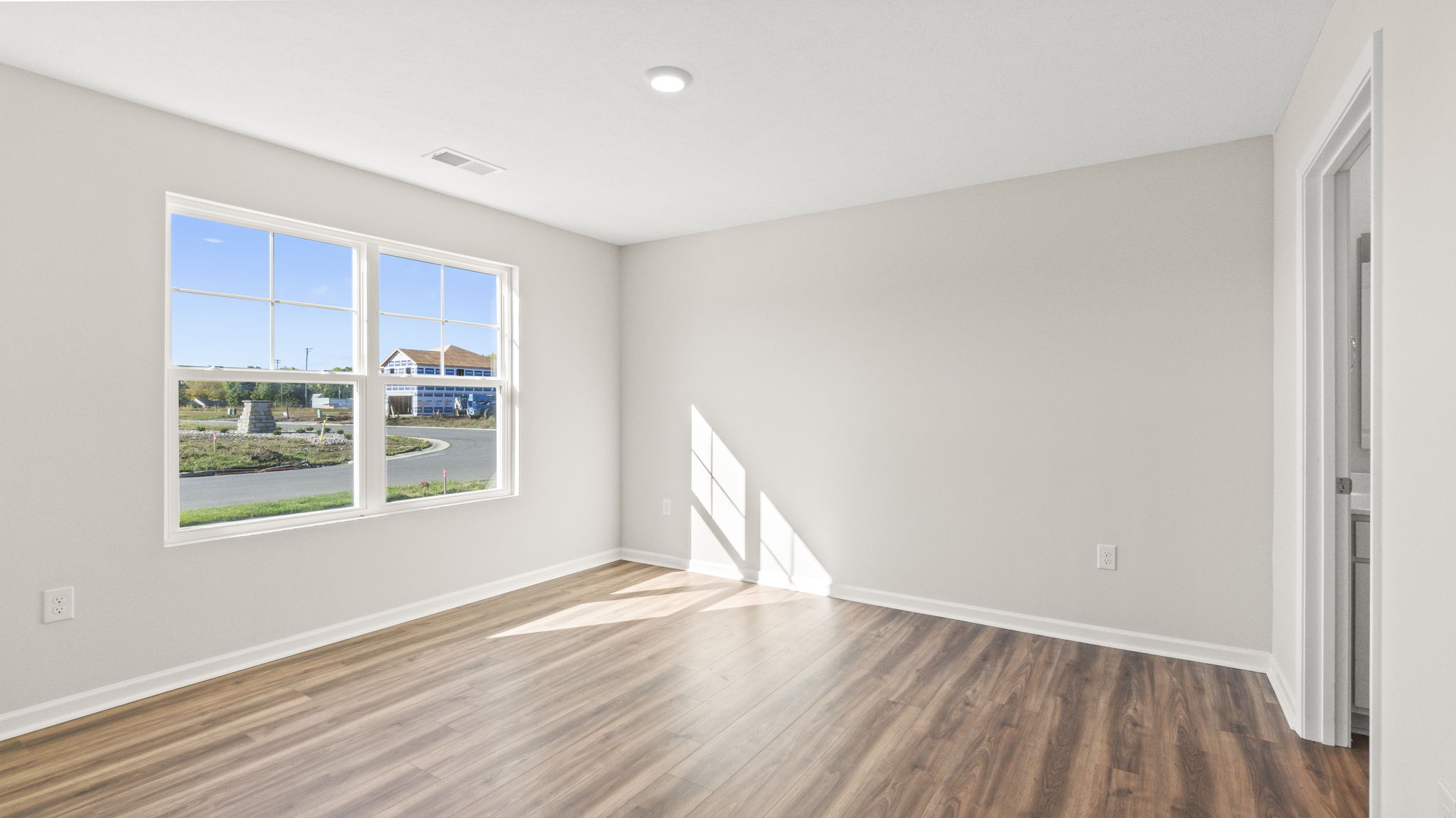 Primary bedroom with wood flooring, white painted walls, and window