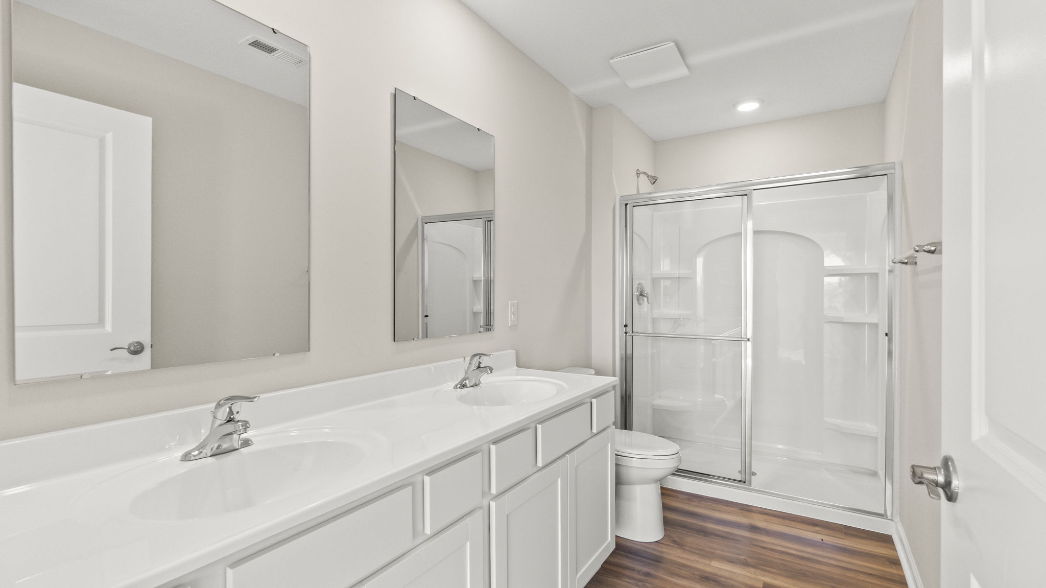 Primary bathroom with double sink vanity, white cabinetry, and walk-in shower