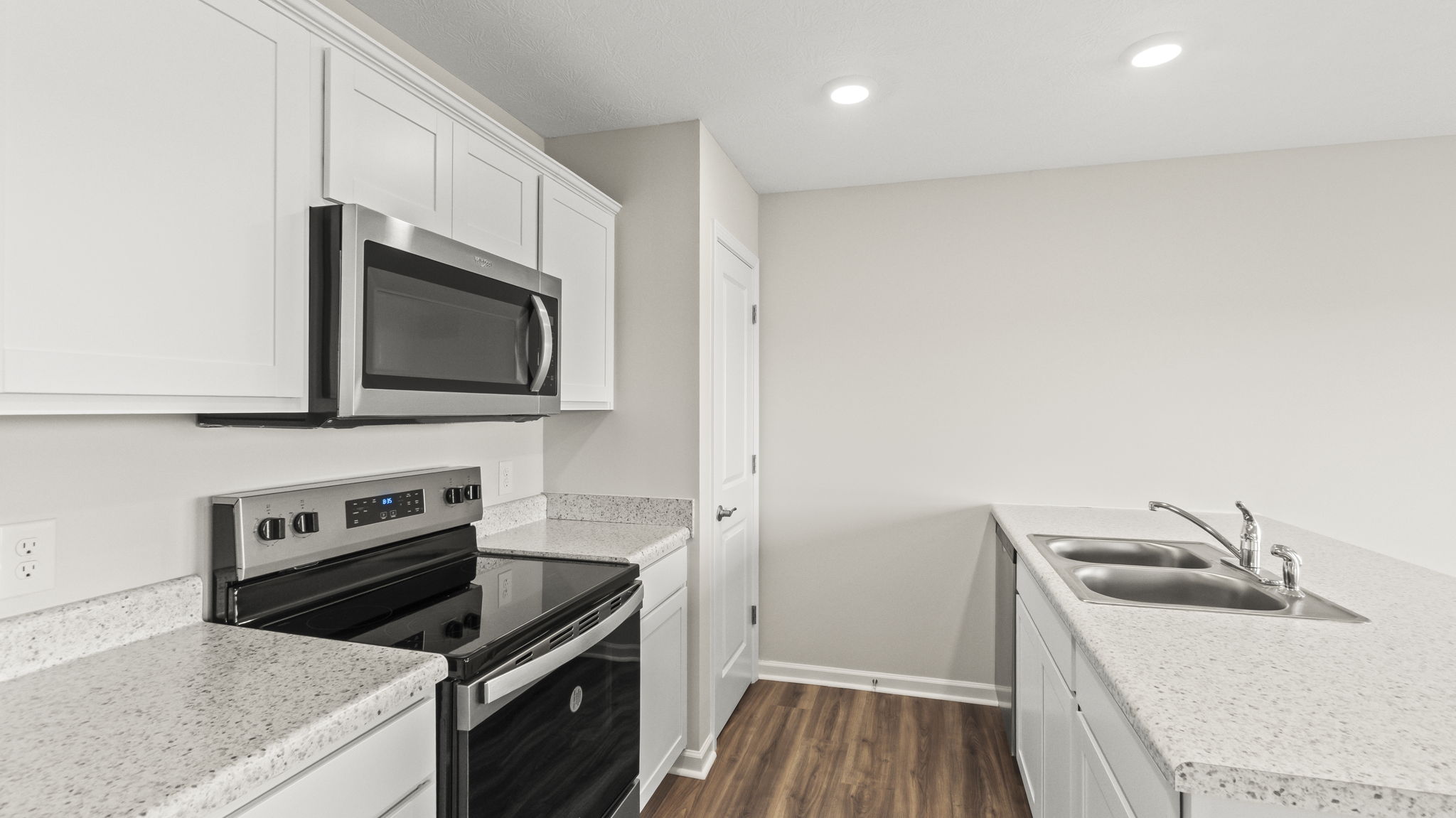 Quarter angle of kitchen with appliances, countertops, white cabinetry, and sink