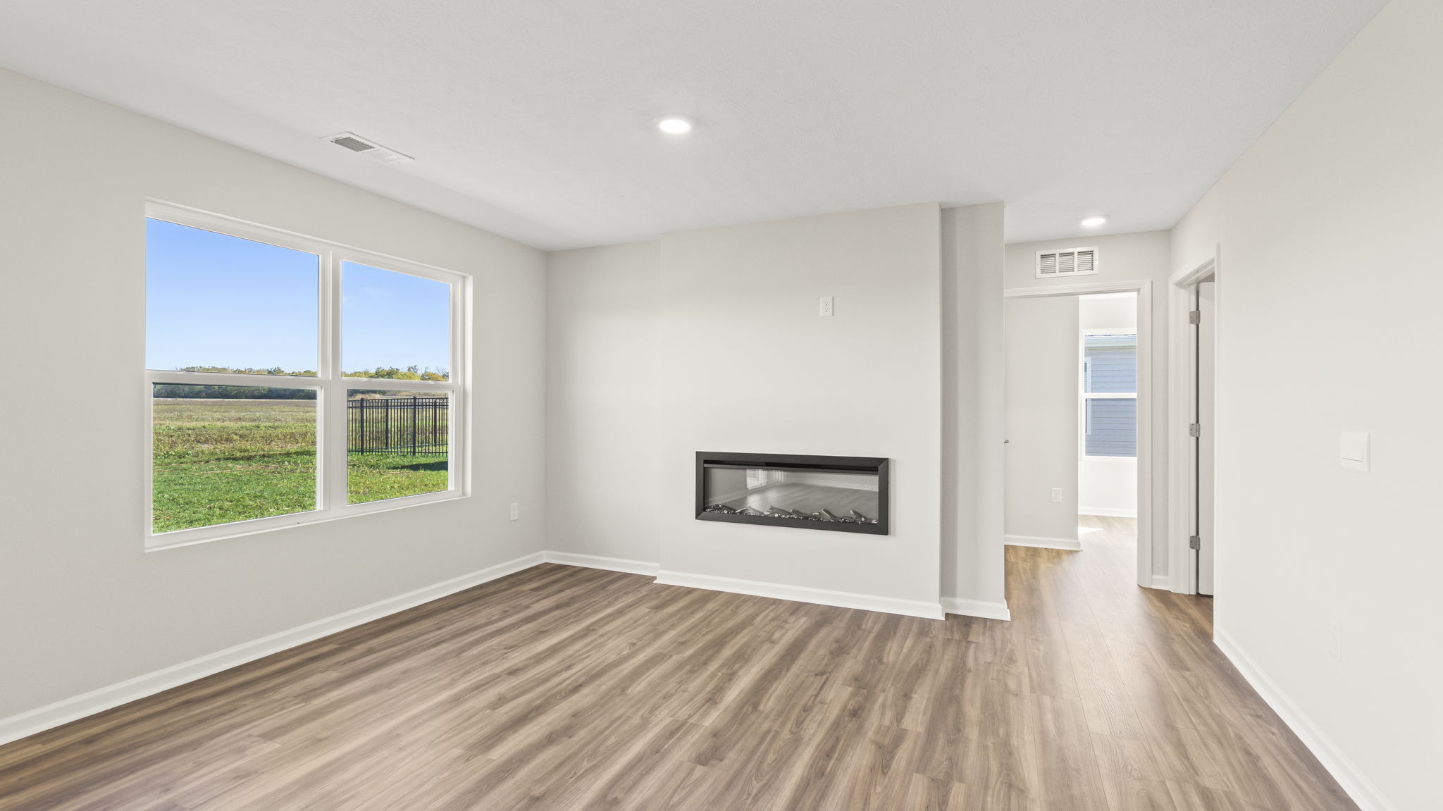 Great room with window to the backyard, electric fireplace, and looking into bedroom
