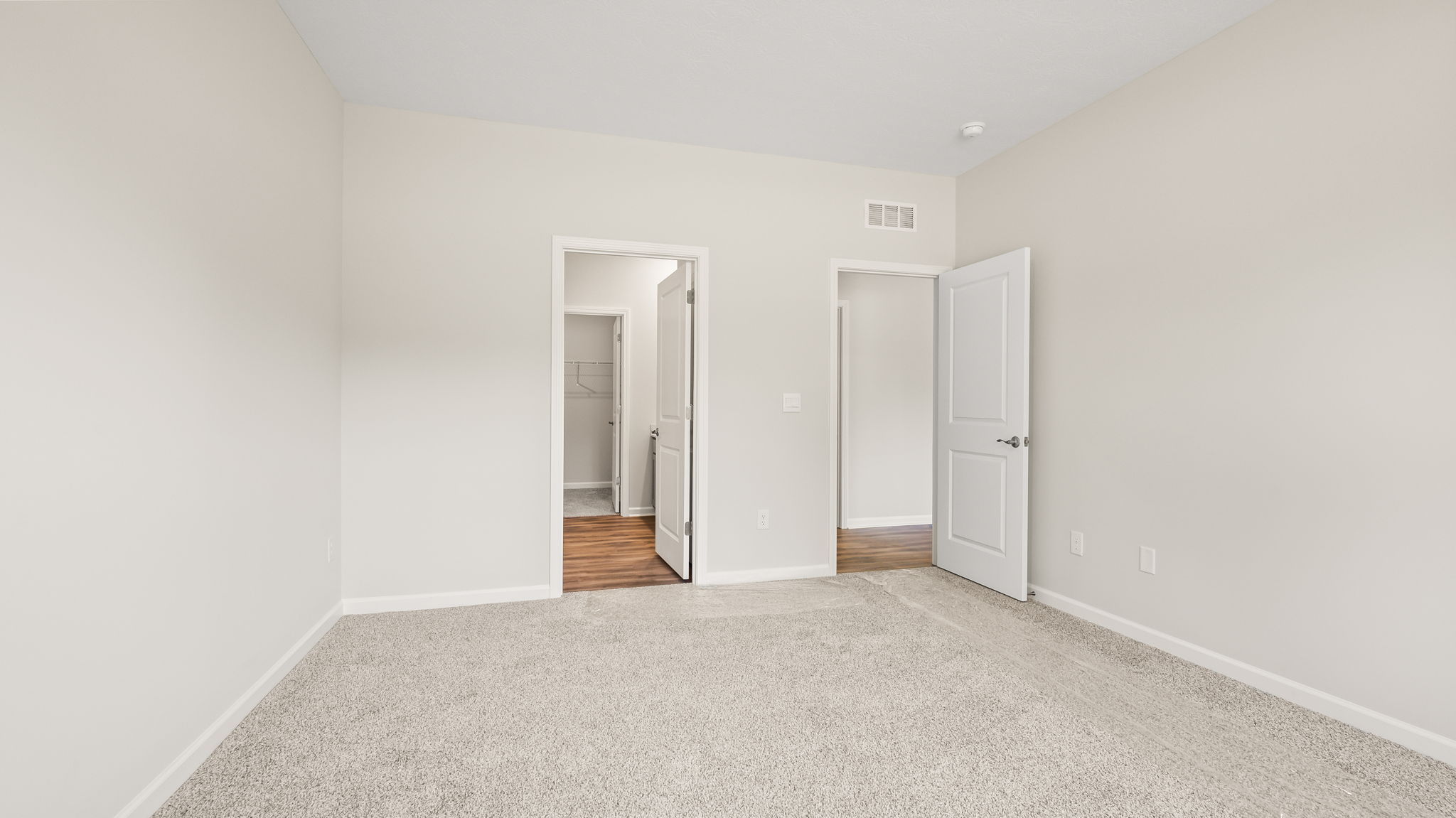 Carpeted primary bedroom with doors to hallway and bathroom suite