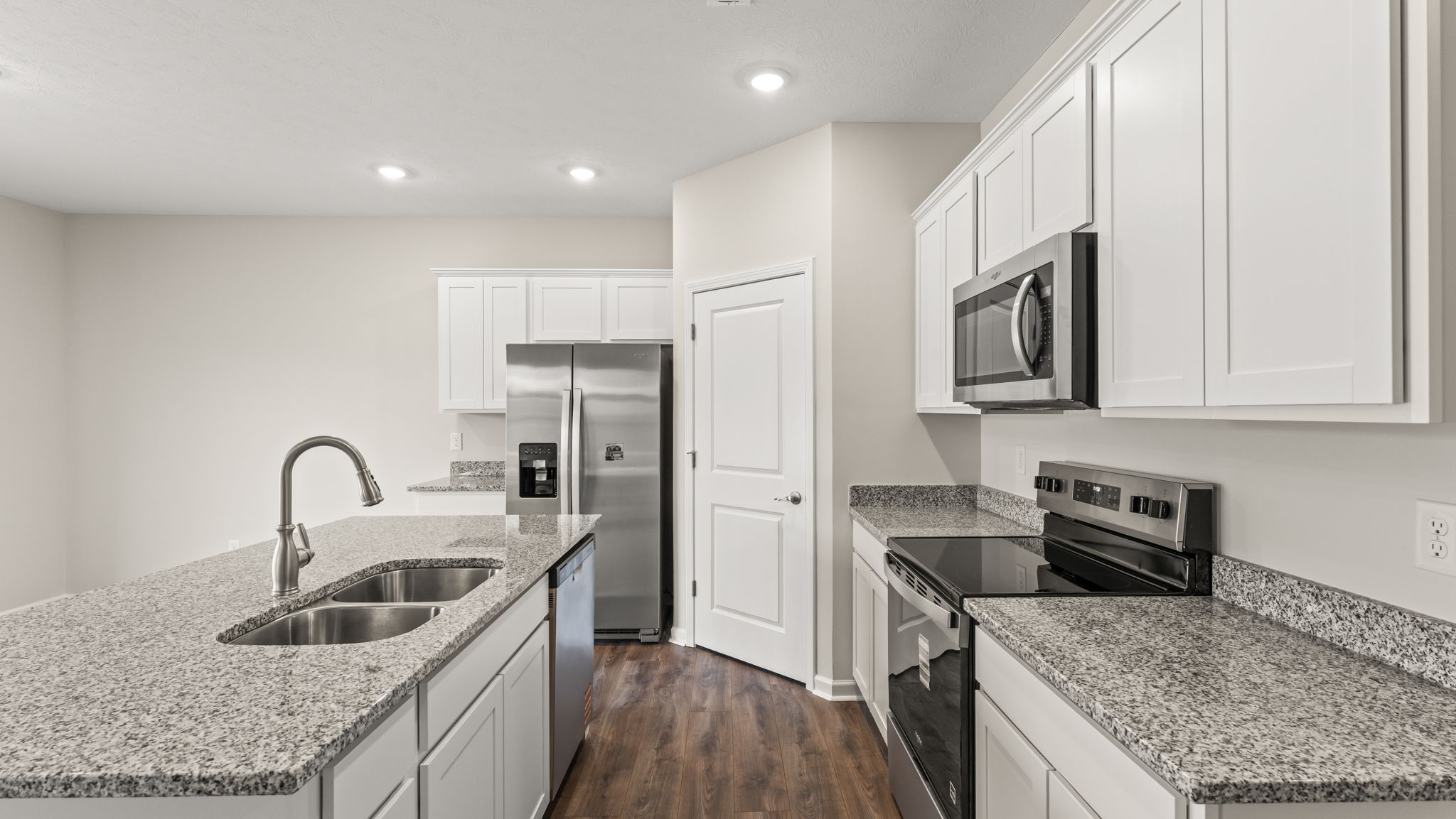 Side view of kitchen with island on the left, pantry in the center, and cabinetry/oven range on the right.