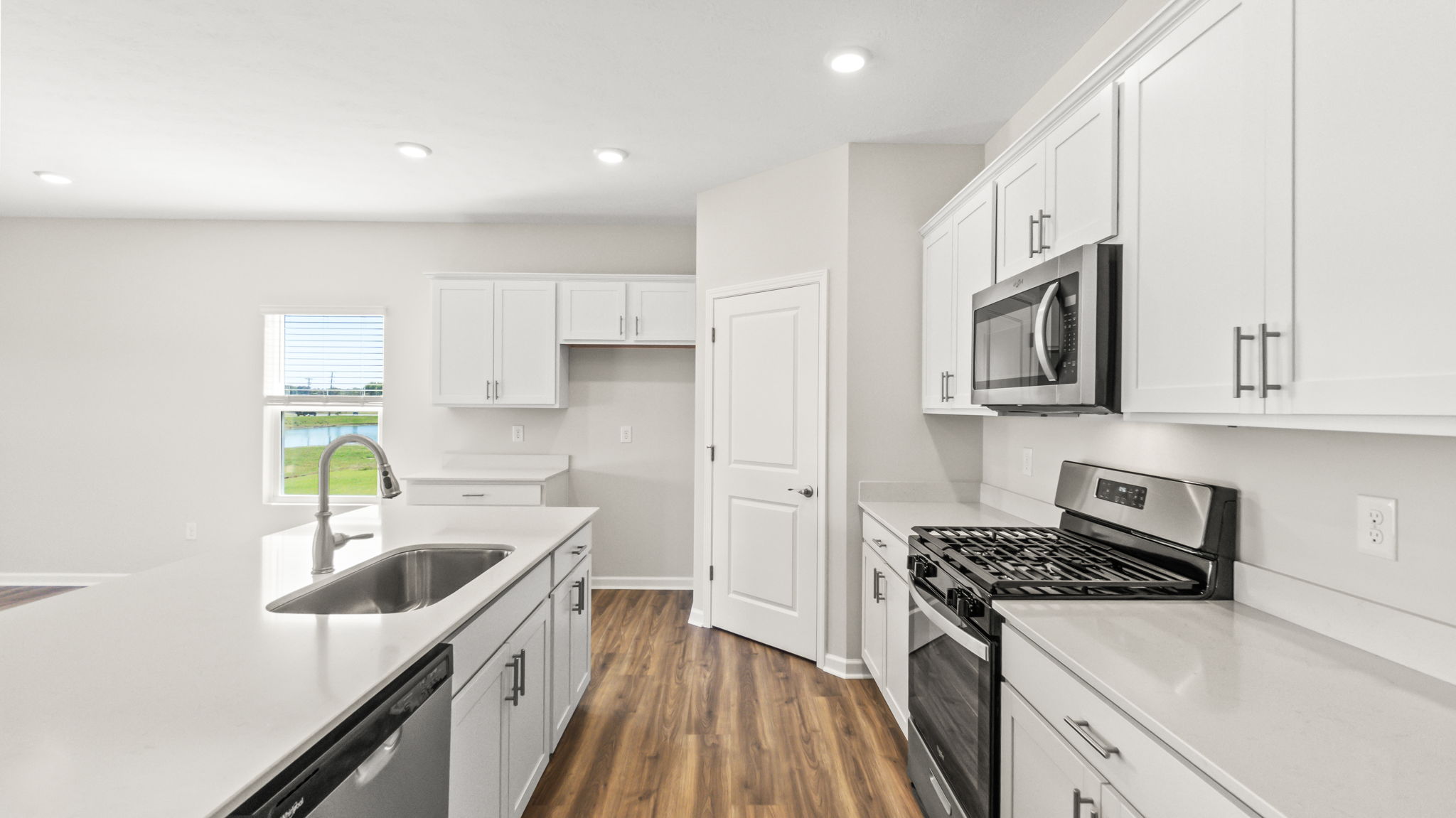 side view of kitchen with island on the left, pantry in the center, and oven range/cabinets on the right