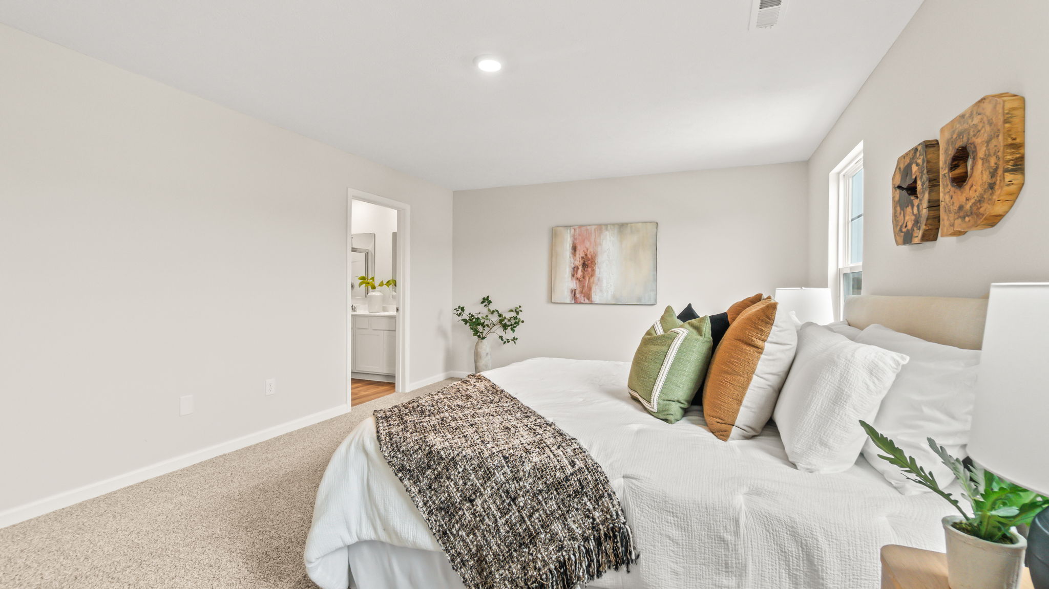 Side view of primary bedroom with mattress adorned with white bedding, throw pillow, and door to primary bathroom suite