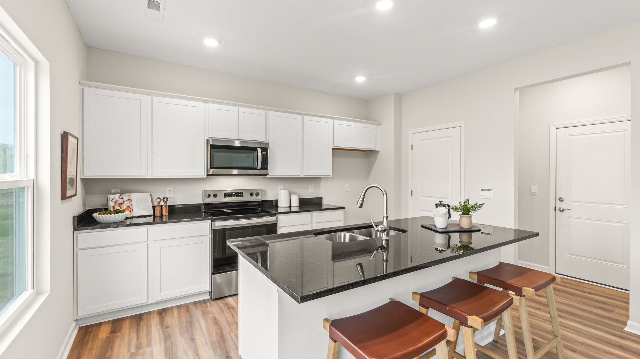 Full view of modern kitchen with white cabinetry, granite countertops, oven range with microwave and stools in front of the island
