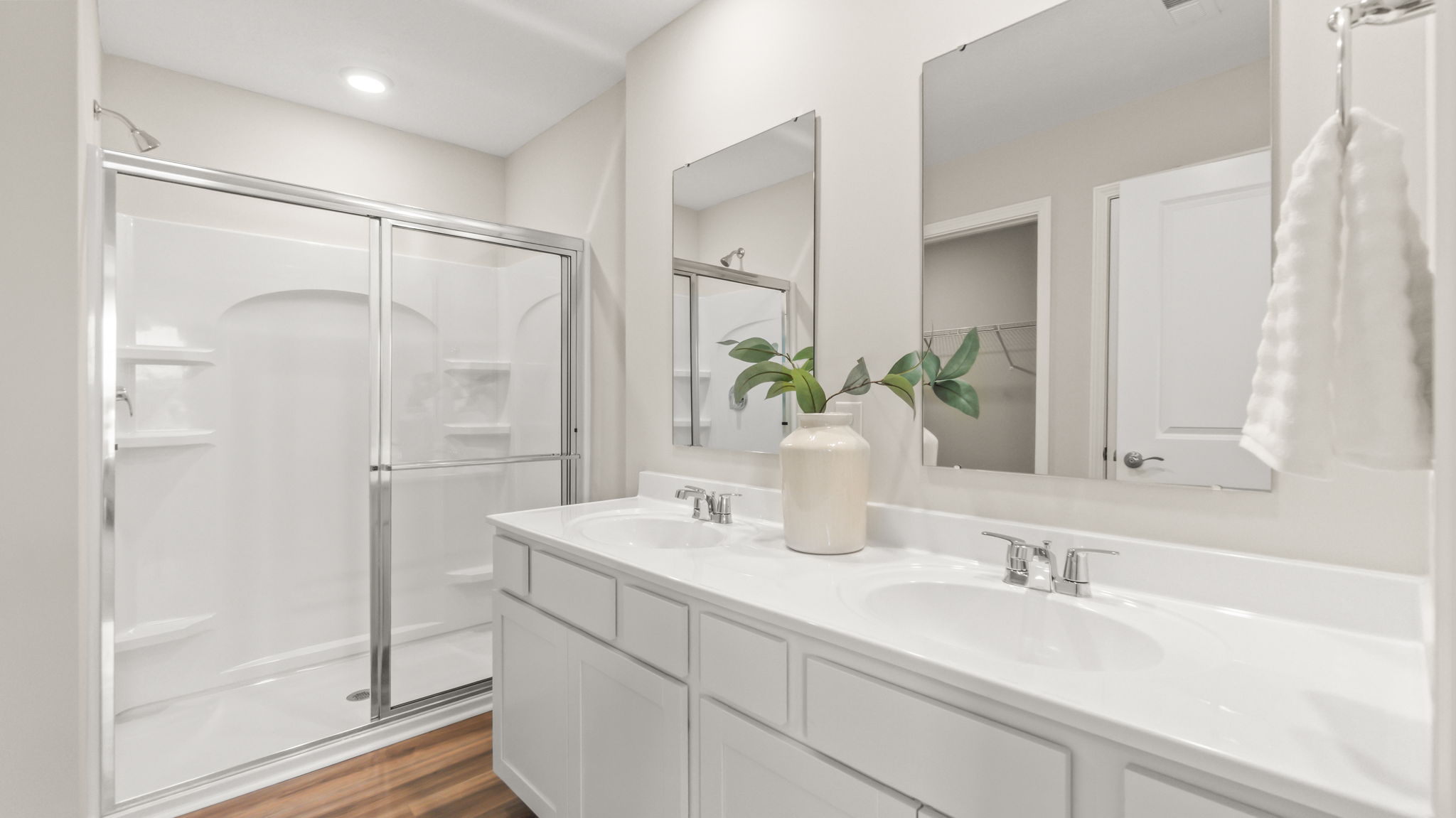 Primary bathroom suite with glass shower door, mirrors, and dual sink vanity