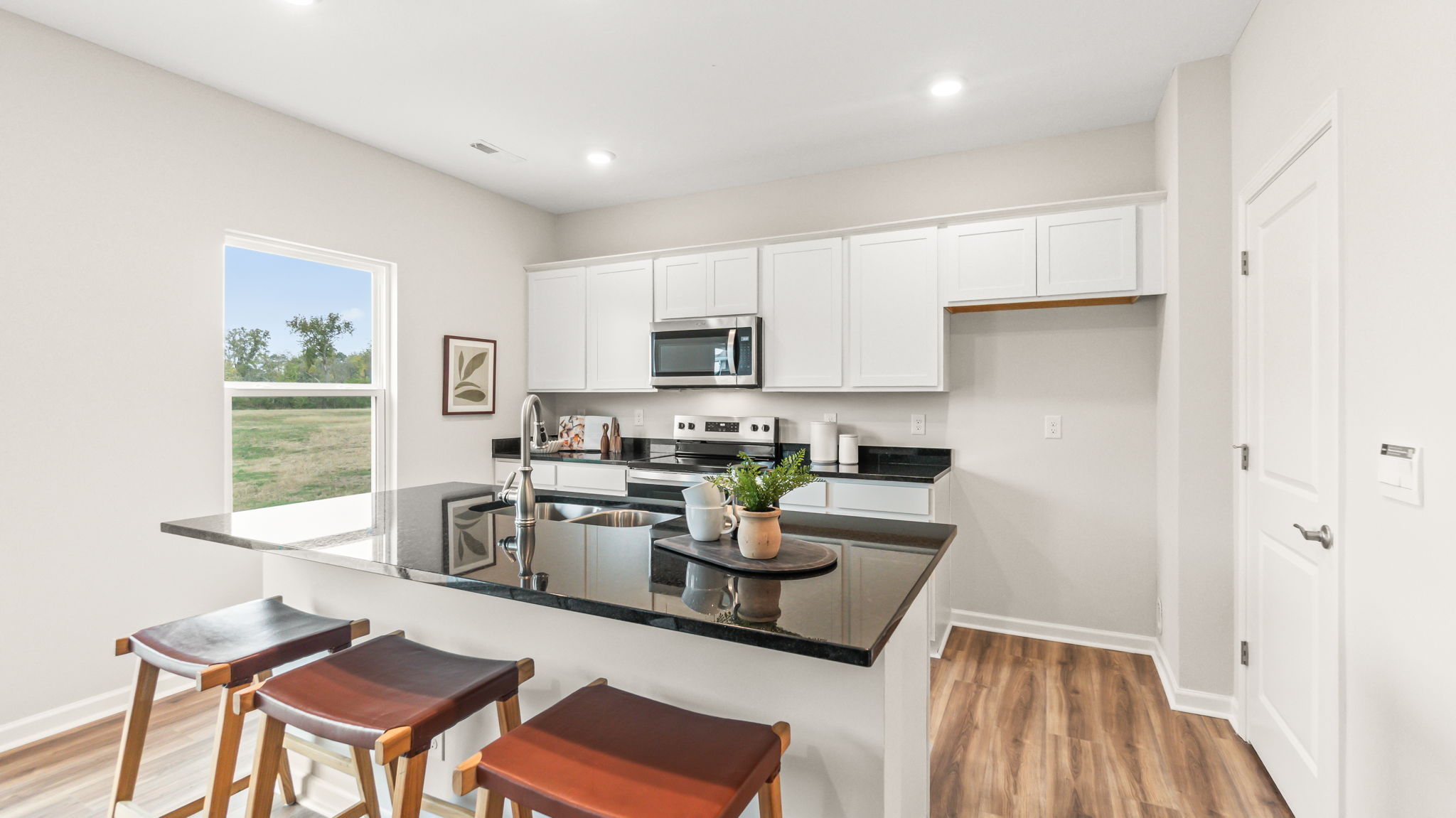 Full view of modern kitchen with white cabinetry, granite countertops, oven range with microwave and stools in front of the island