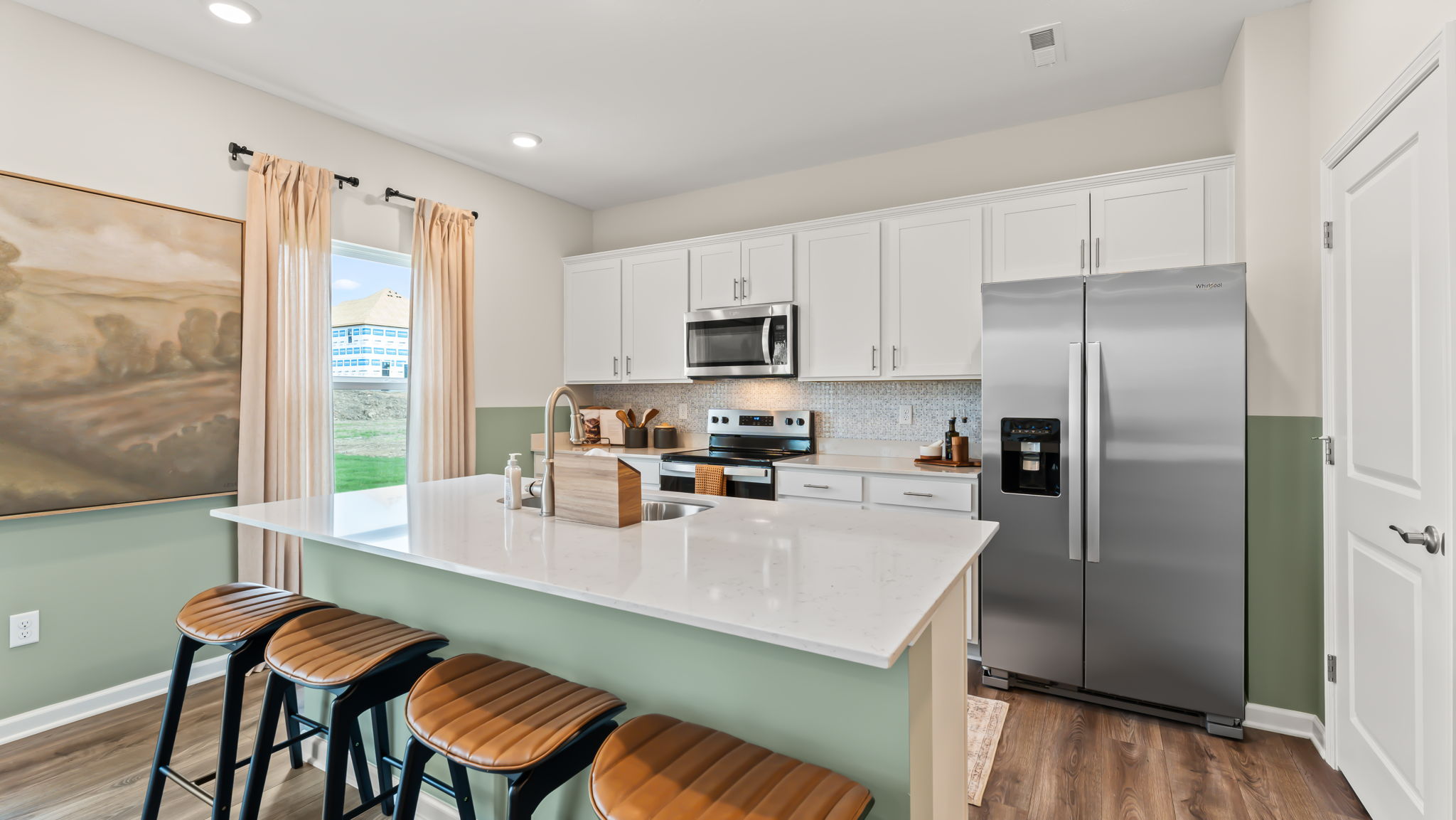 wide angle three-quarter image of modern kitchen with white countertops, stainless steel appliances, white cabinetry, and lots of natural lighting contrasting the green paint