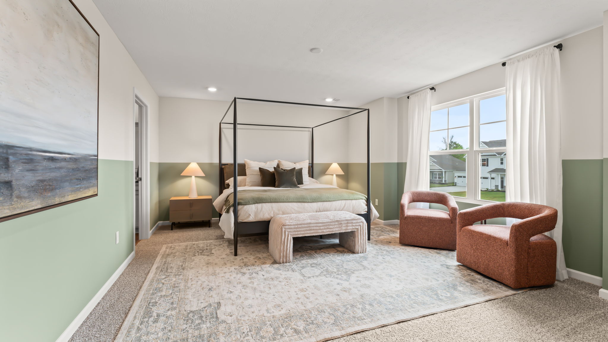 Primary bedroom with pale green half-wall, burgundy textured chairs, and large cozy bed