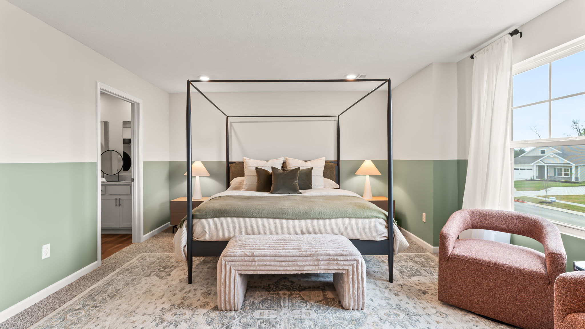 Closeup of primary bed with metal box frame, ottoman, and door to primary bathroom