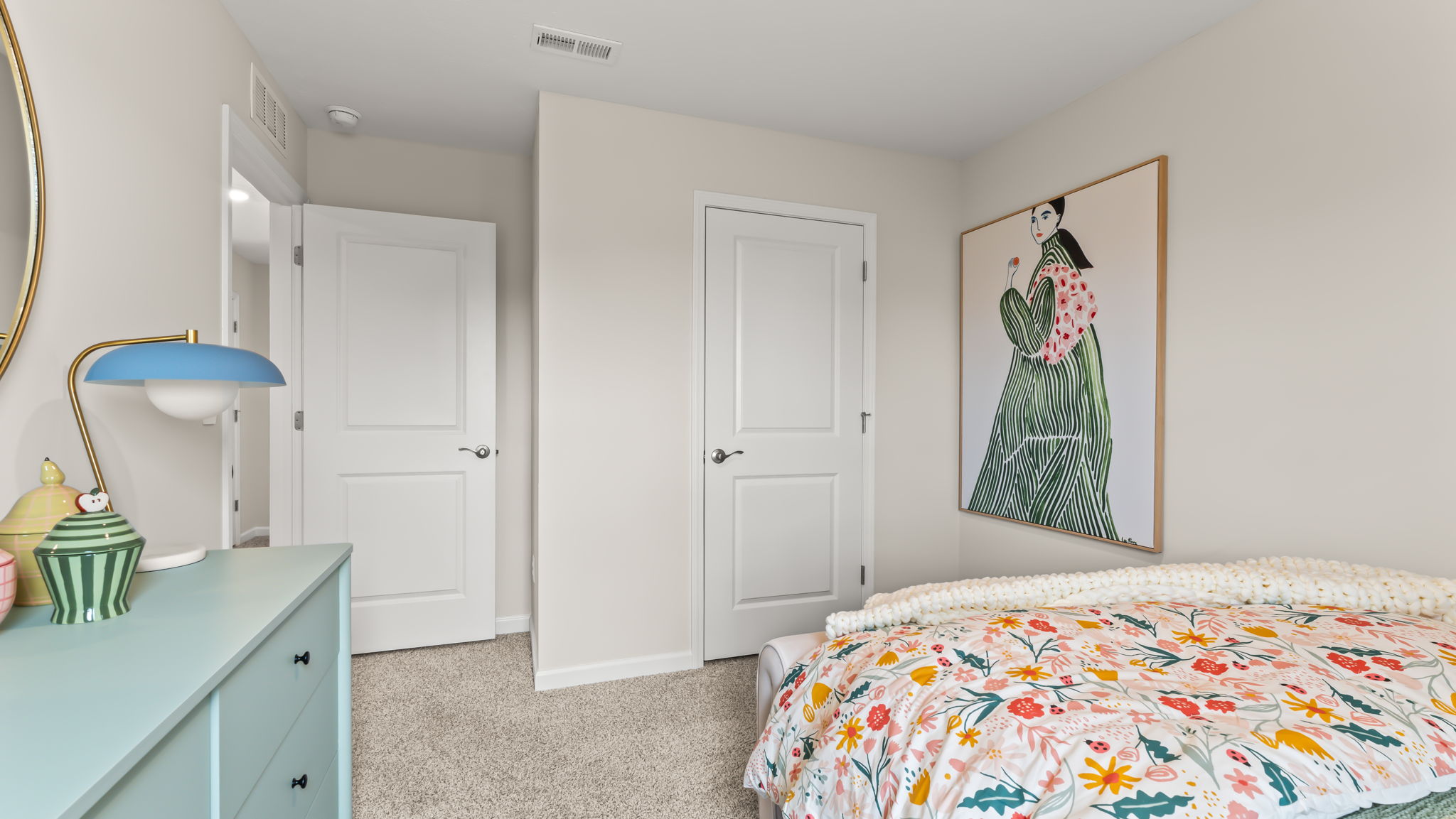 Bedroom with green desk and colorful bed next to artwork with feminine form and closet