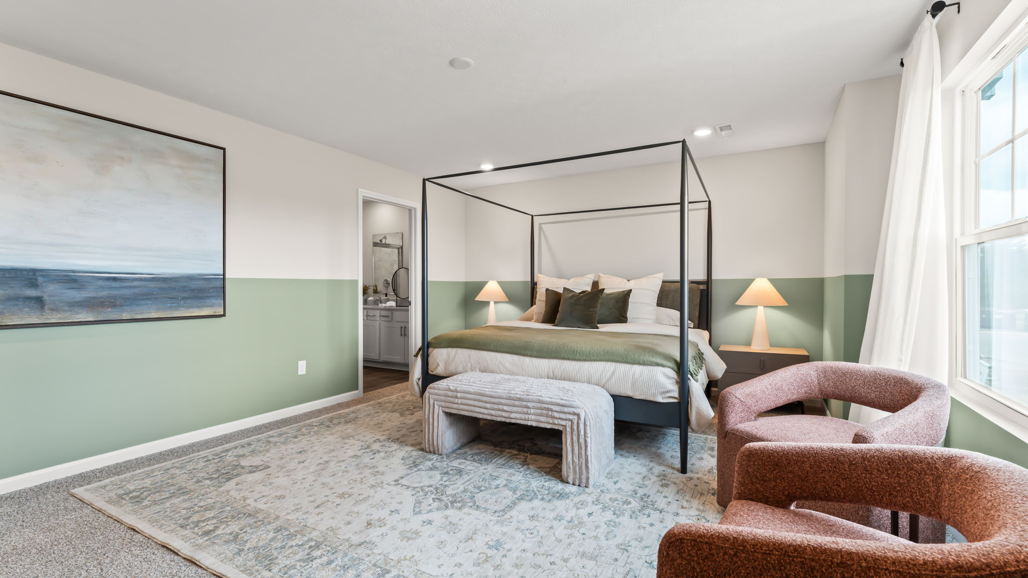 Primary bedroom with pale green half-wall, burgundy textured chairs, and large cozy bed