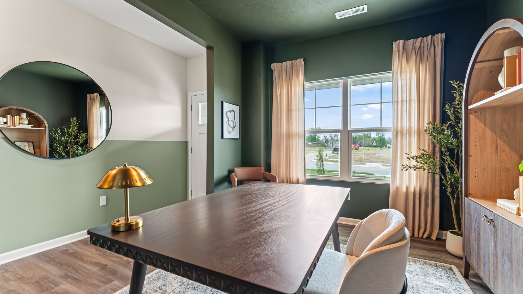Flex room with deep green walls arranged as an office with wooden bookshelf and table