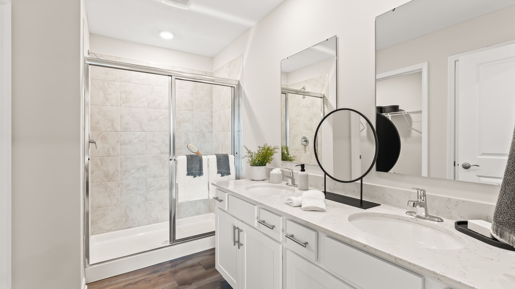 Primary bathroom suite with glass shower door and dual-sink vanities