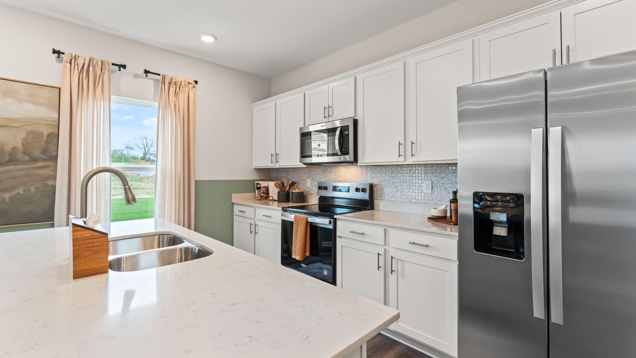 three-quarter image of modern kitchen with white countertops, stainless steel appliances, white cabinetry, and lots of natural lighting contrasting the green paint