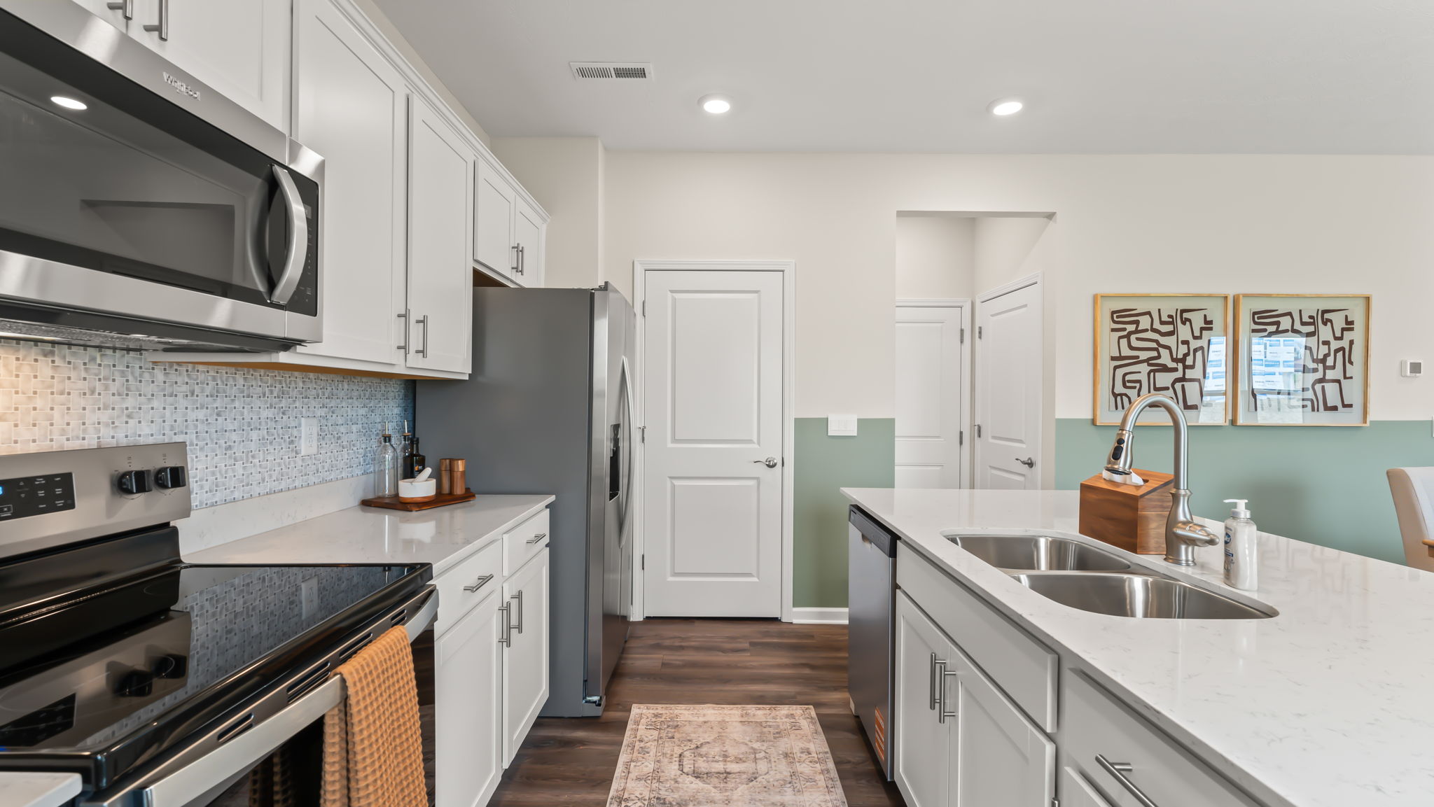 Side view of kitchen with oven range on the left, white cabinetry, and island with sink