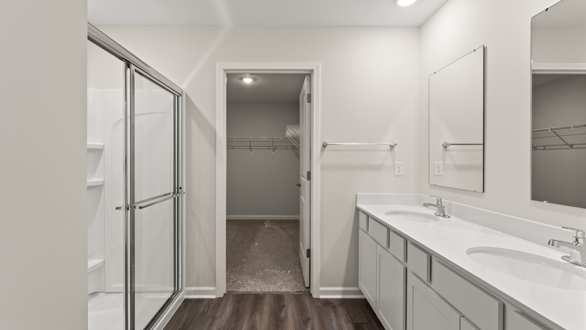Primary bathroom with walk-in shower on the left, walk-in closet in the center, and dual-vanity sink and mirrors on the right.