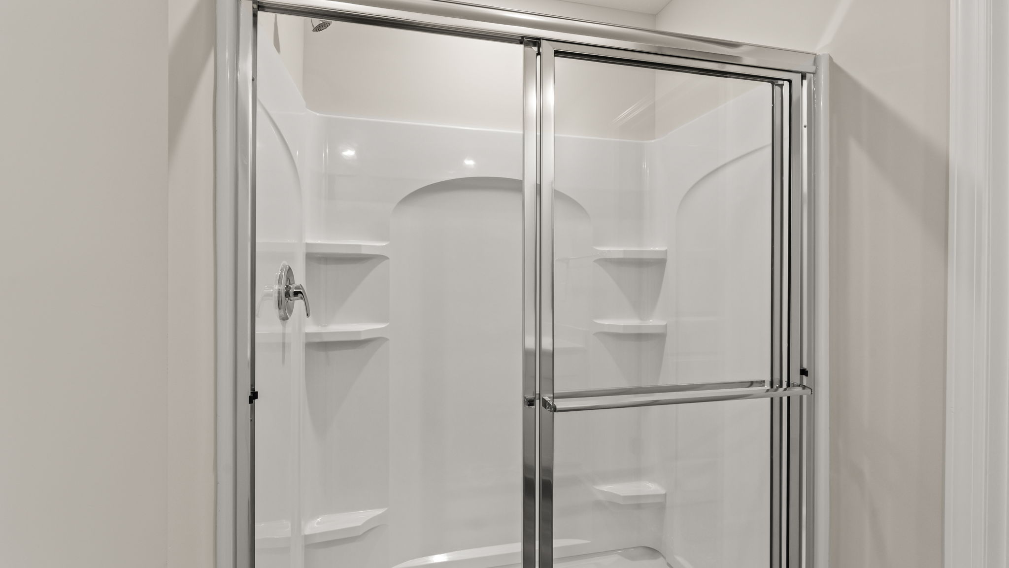 Closeup of walk-in shower with glass door and tiered shelving.