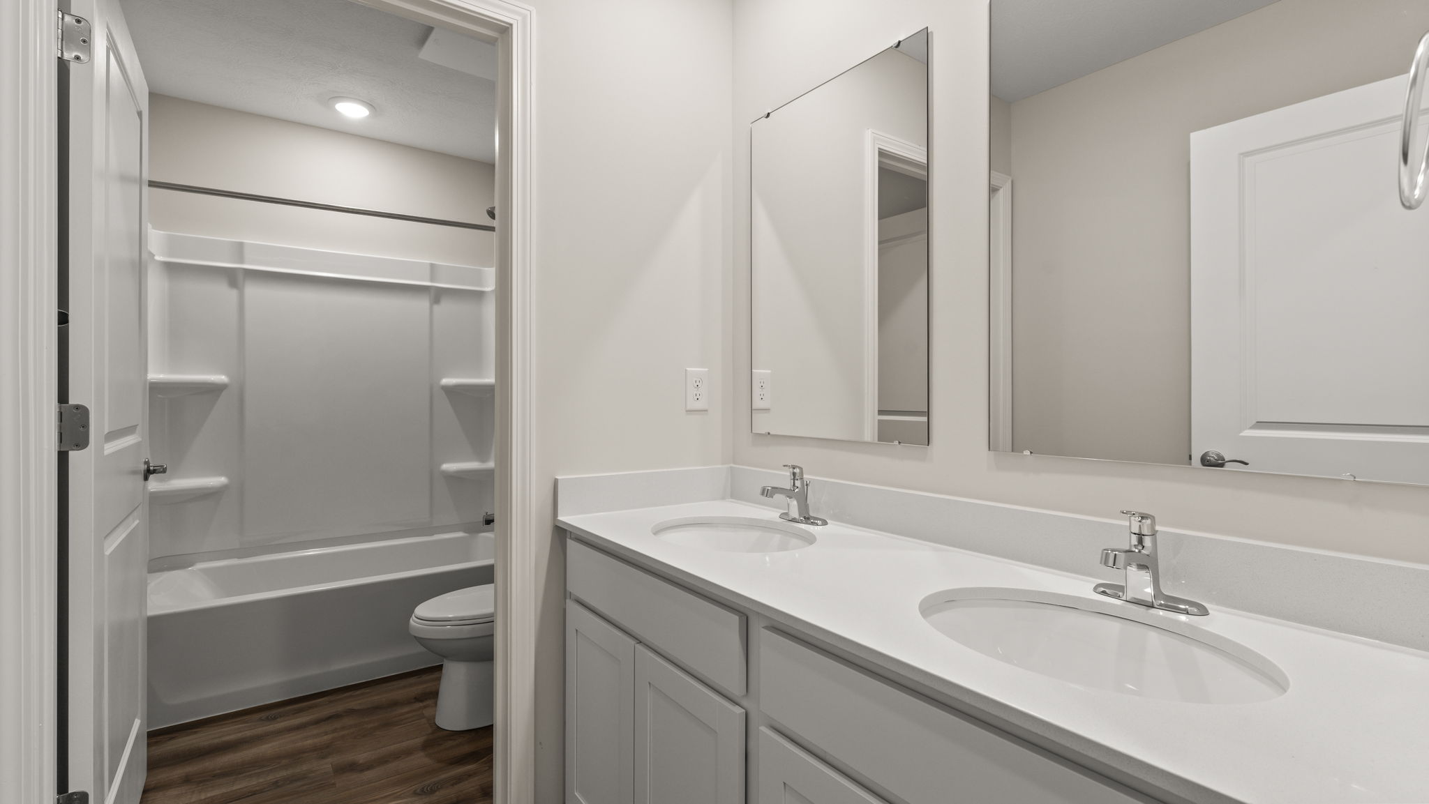 Bathroom with dtwo sinks, mirror, and tub/shower in the back.