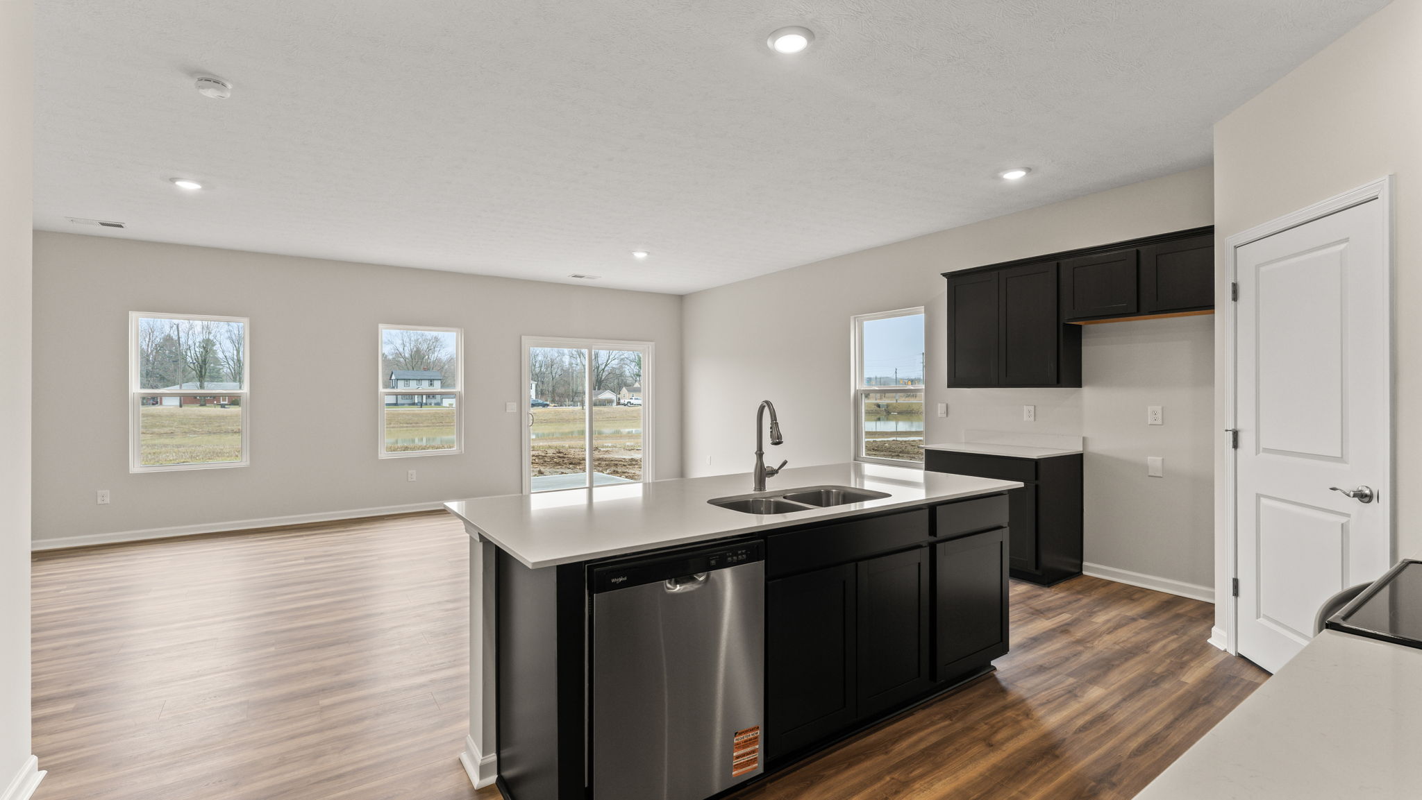 Image of the kitchen from behind the island which includes a dishwasher, sink, and granite countertops