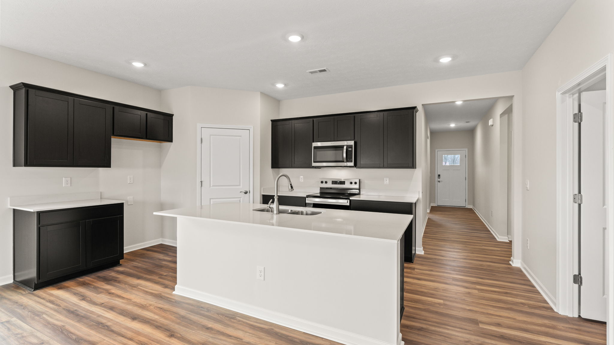 three-quarter view of kitchen with dark cabinets, island, and laminate wood flooring