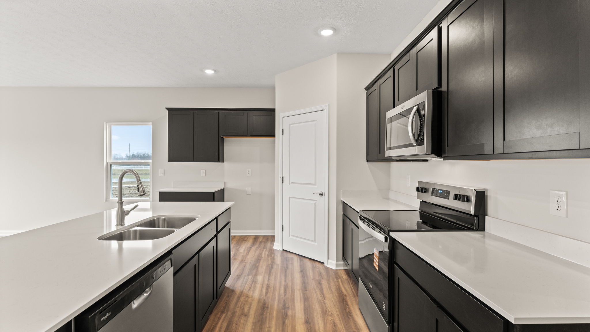 Side view of kitchen with island on the left, pantry in the center, and oven range on the right.