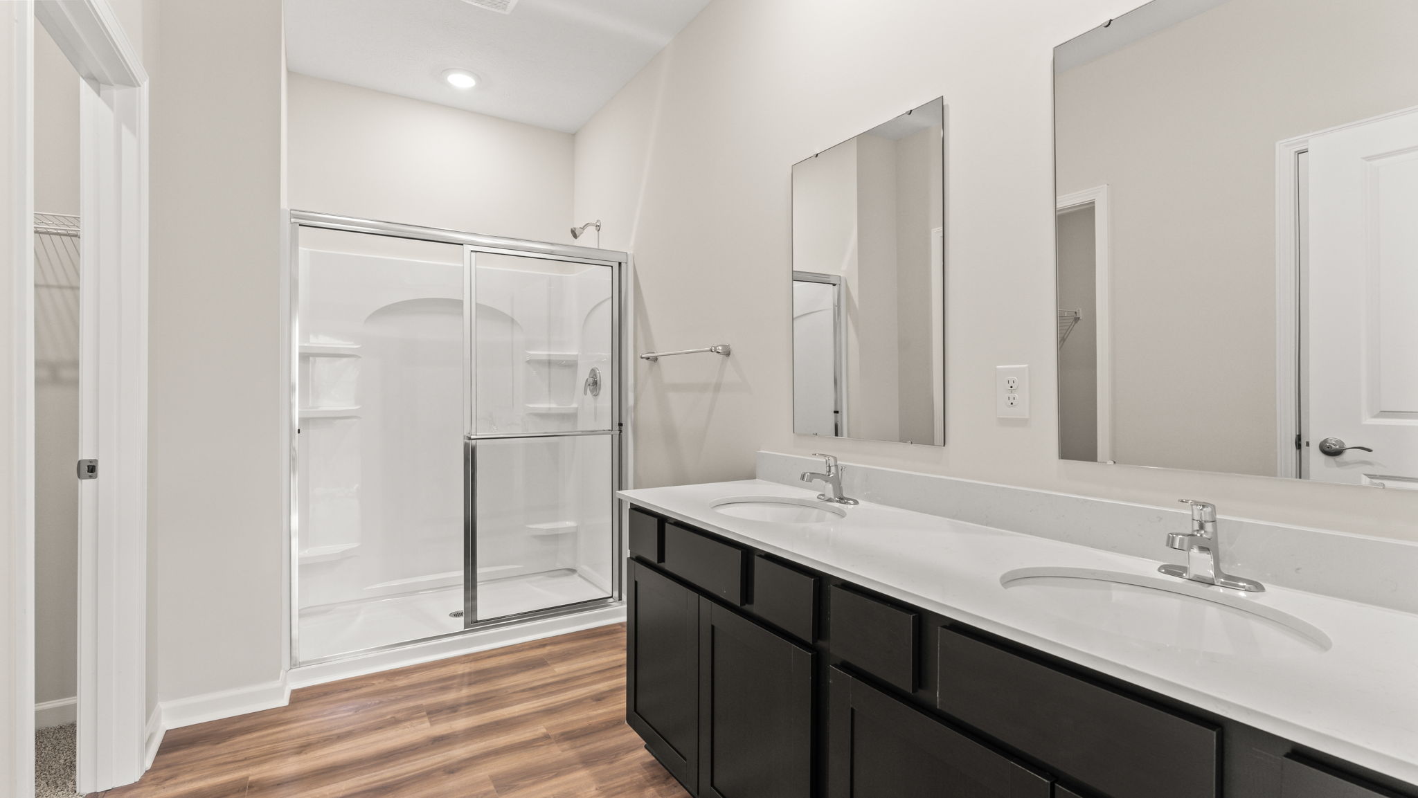Primary bathroom suite with dark cabinets, white countertops, double bowl vanity, and walk-in shower.