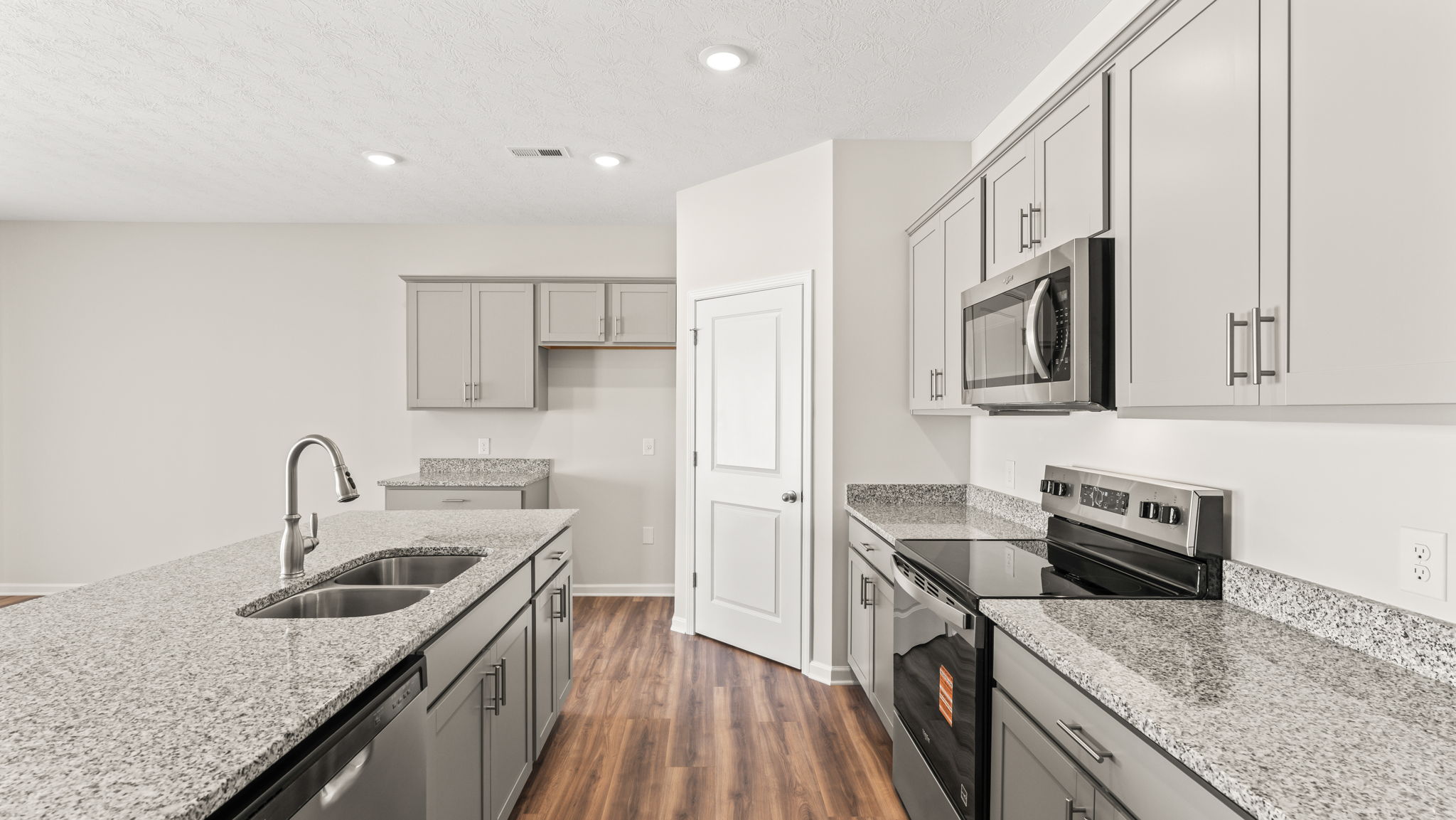 Side view of kitchen with island on the left, pantry in the center, and oven range on the right.