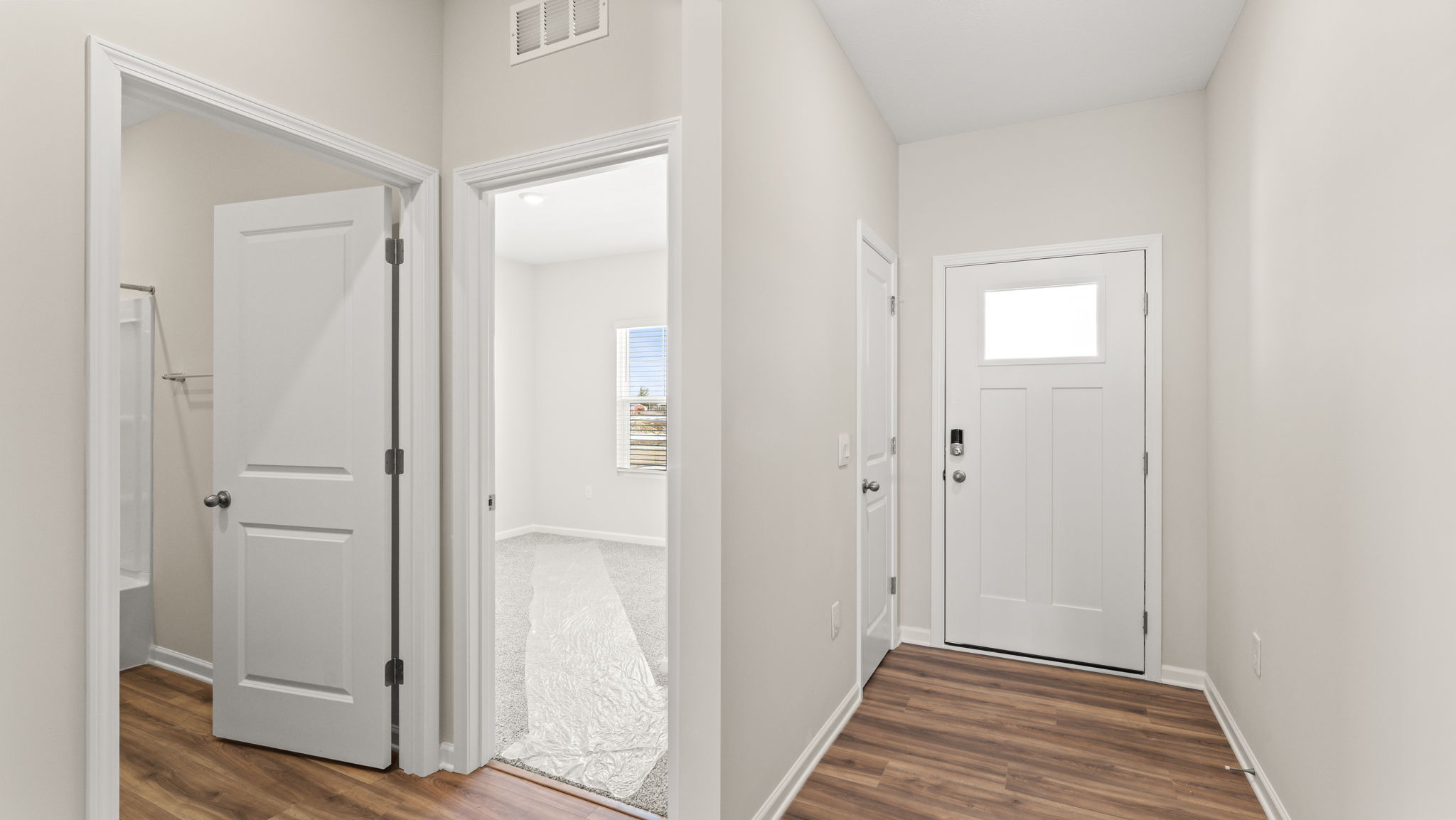 Wide angle of the front of the home with bathroom on the left, bedroom in the center, and front door on the right.