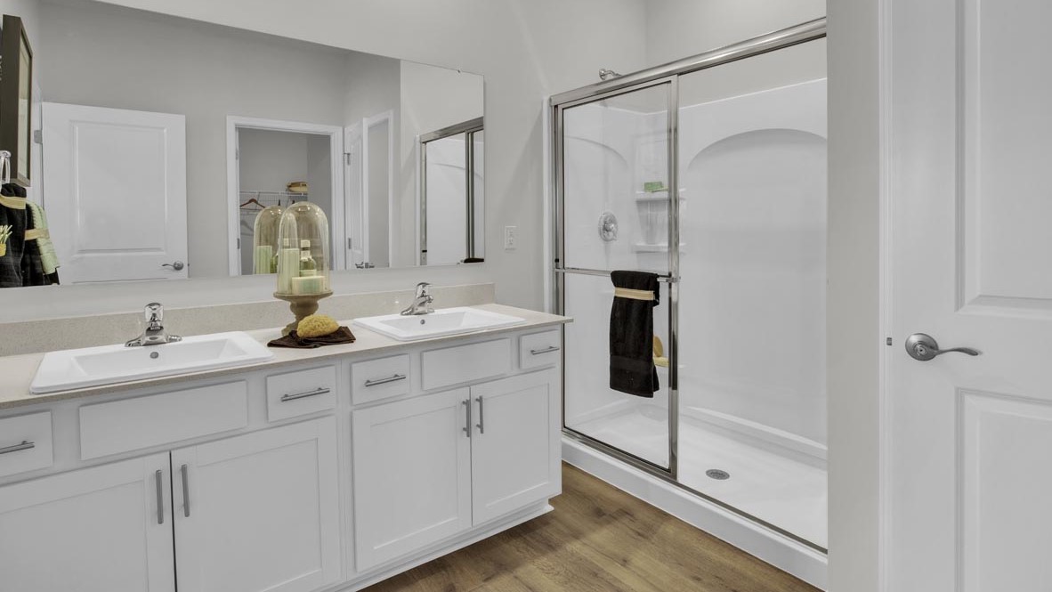Primary bathroom with dual vanity sinks, white cabinets, and walkin shower with sliding door.