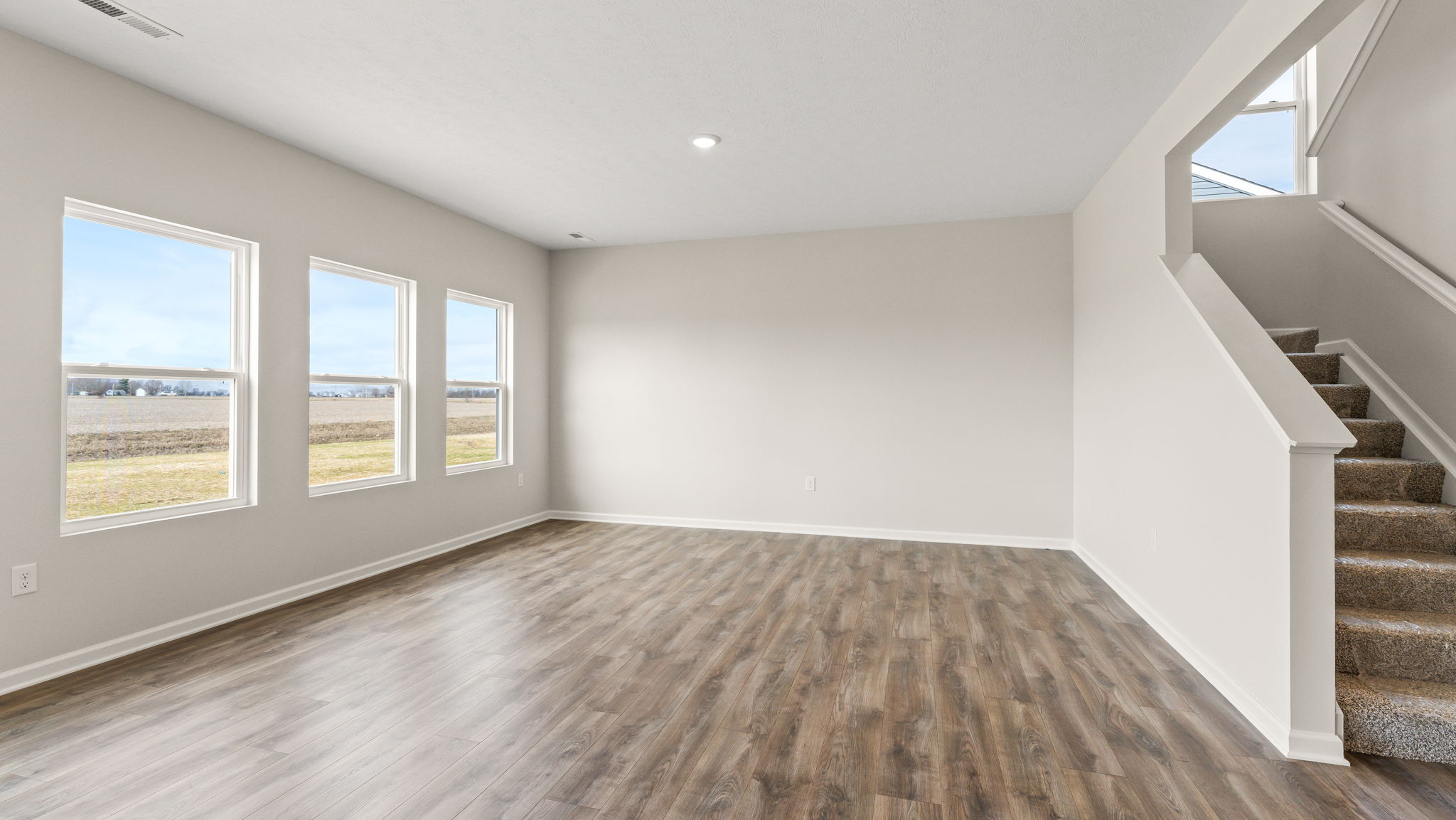 Full living room with view of stairs and three windows to the outside.