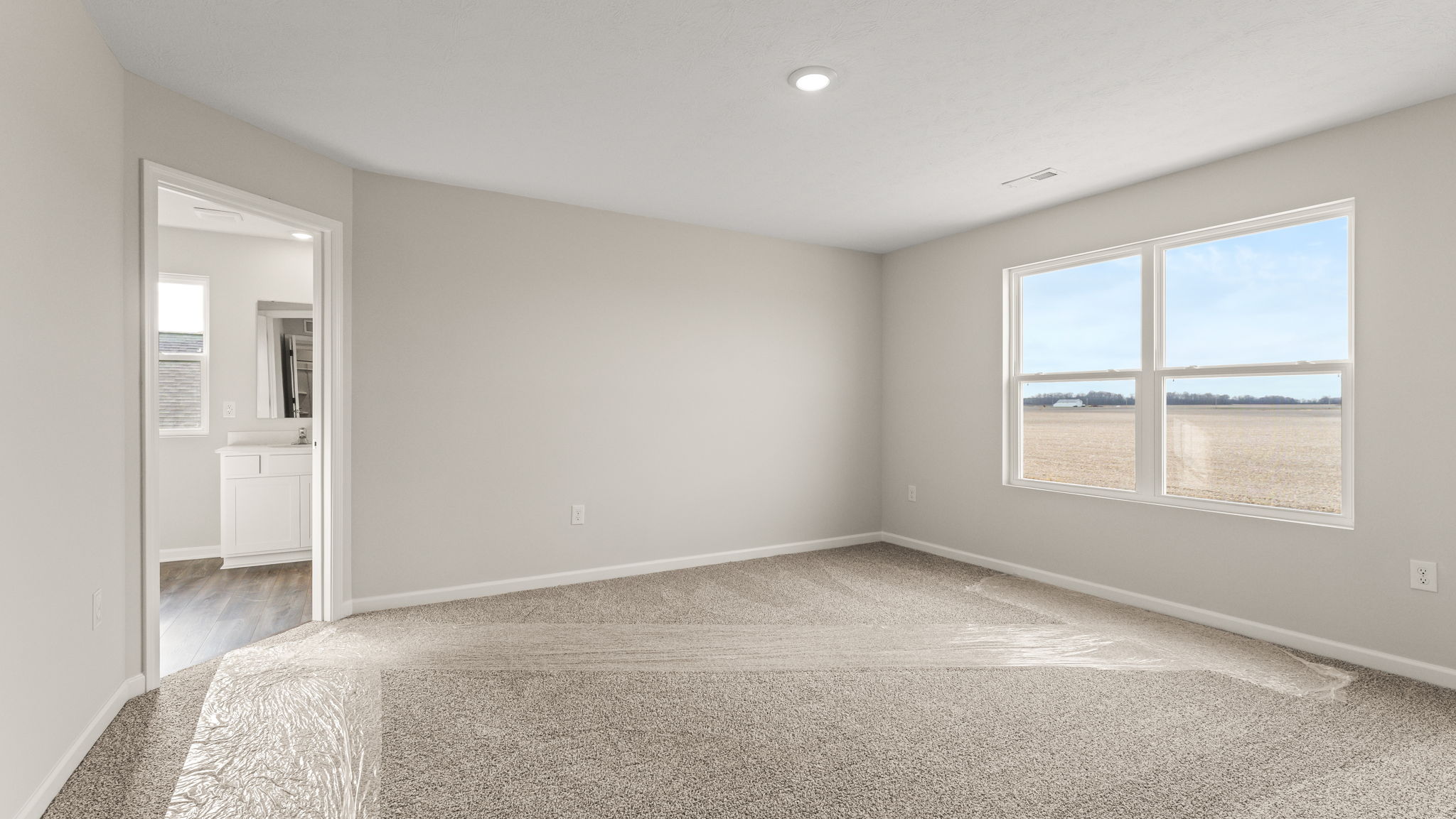 Primary bedroom suite with carpet, view of primary bathroom, and window.