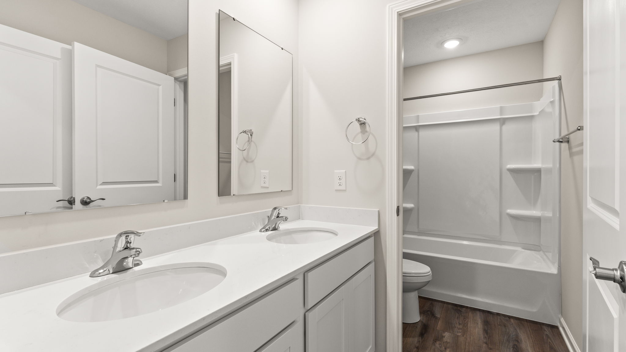 Bathroom with double sink and mirror and shower in the background.