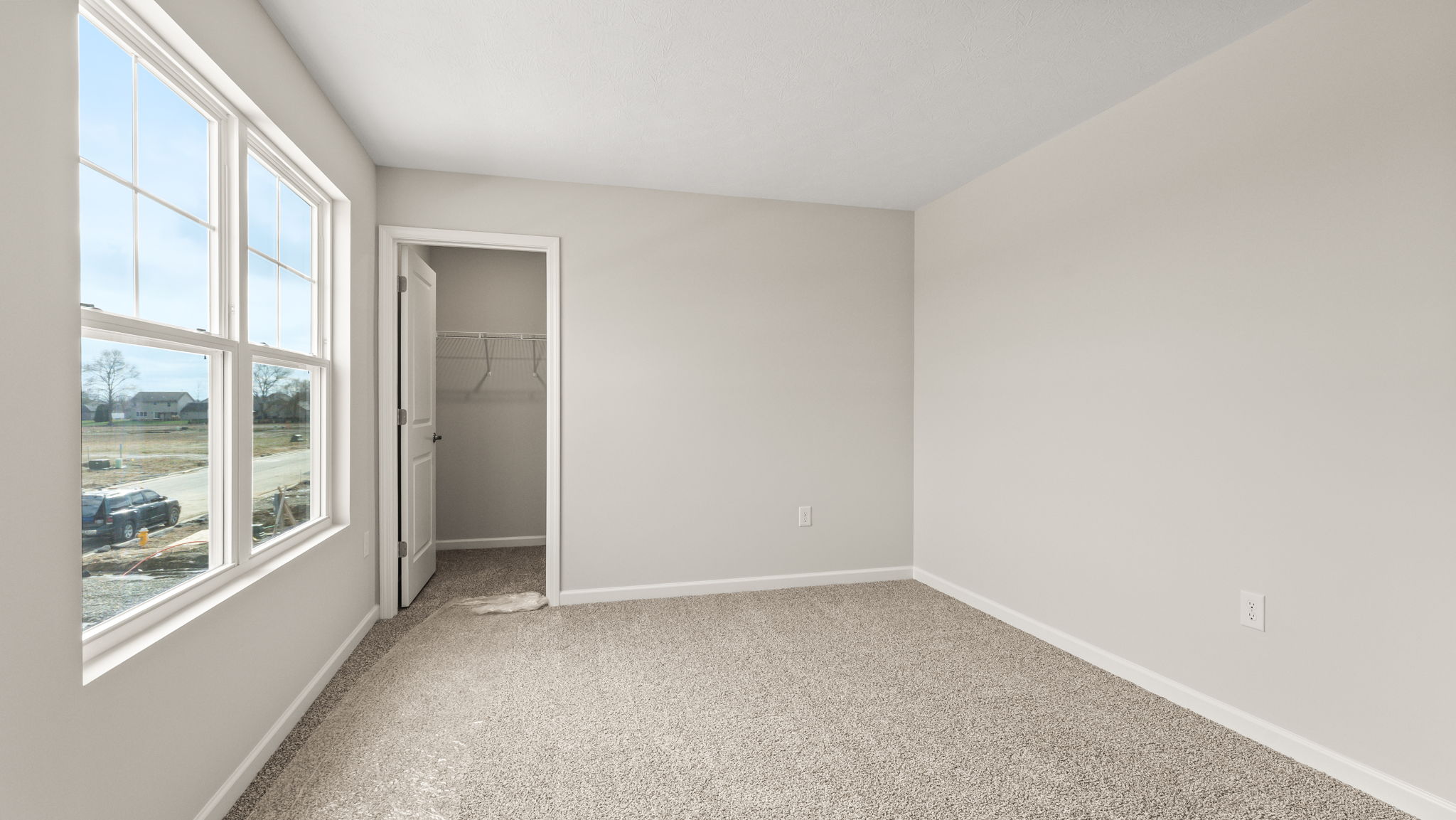 Carpeted bedroom with window to the outside on the left and walk-in closet straight on.