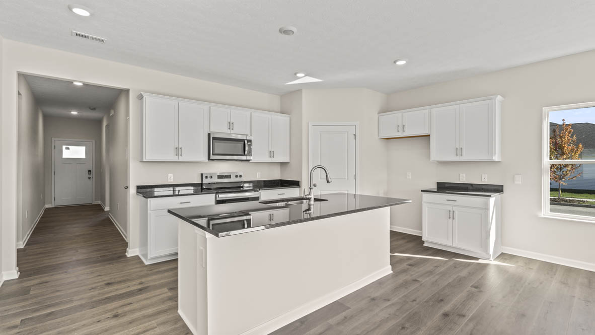 View of the full kitchen, appliances, white cabinets, and front door through hallway.