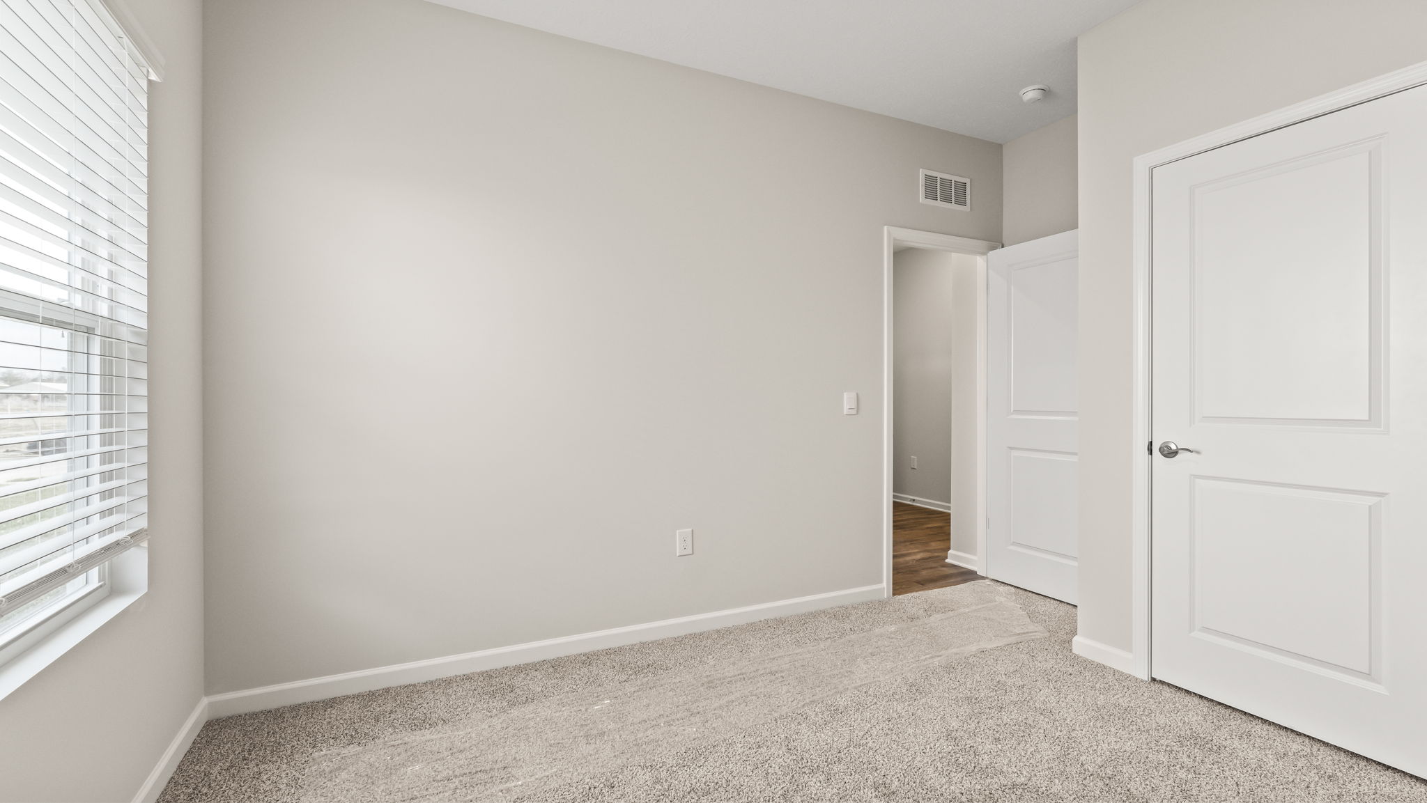 Carpeted bedroom with white walls, closet, and door to hallway.
