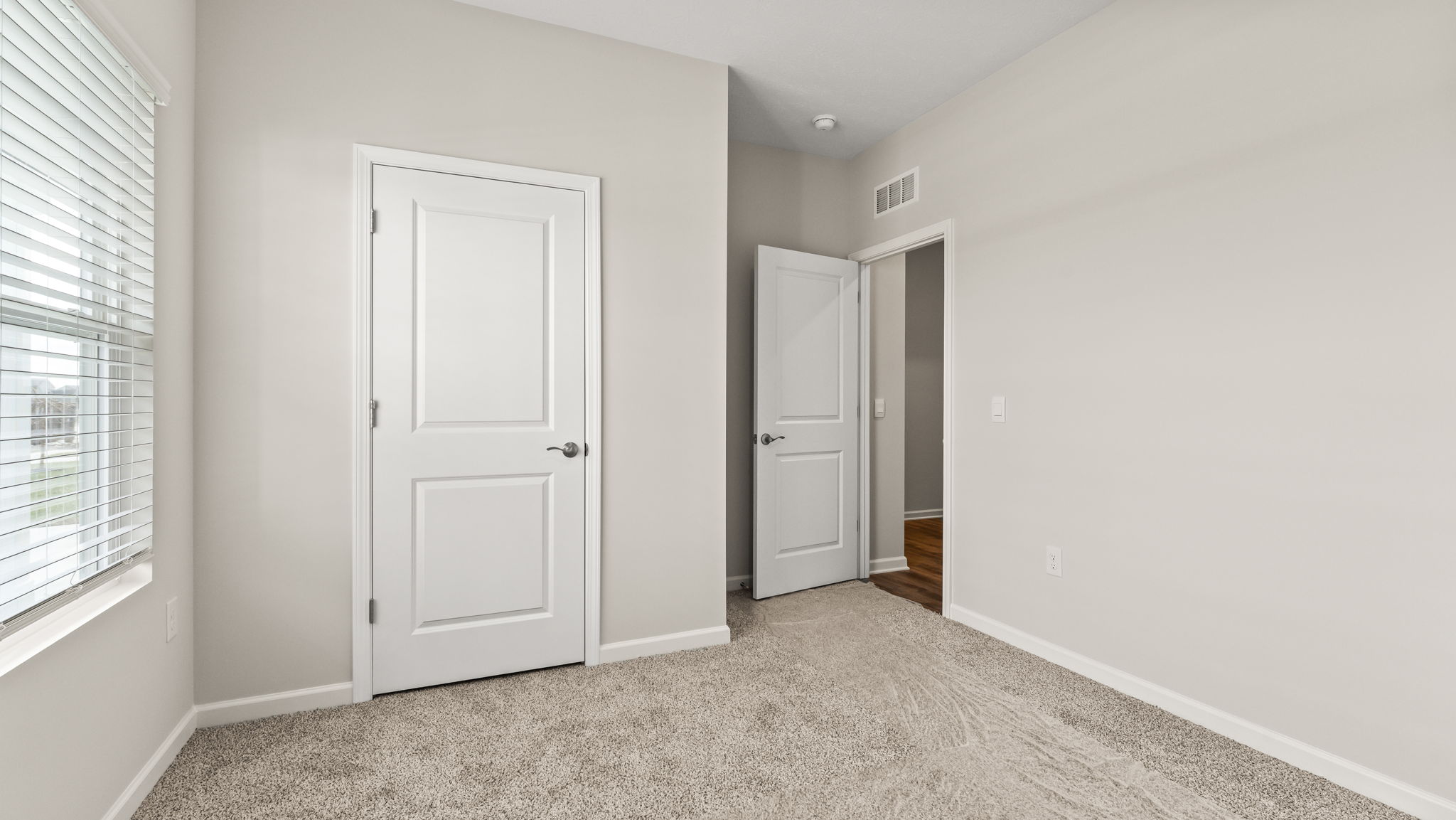 Carpeted bedroom with white walls, closet, and door to hallway.
