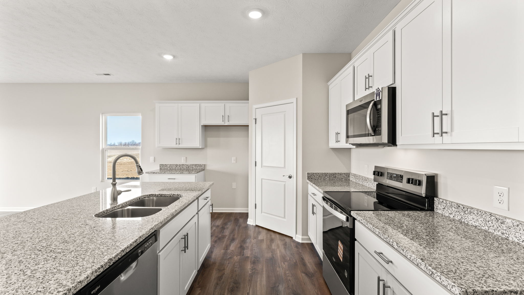 Side view of kitchen, island, sink, oven range, pantry, and cabinetry.