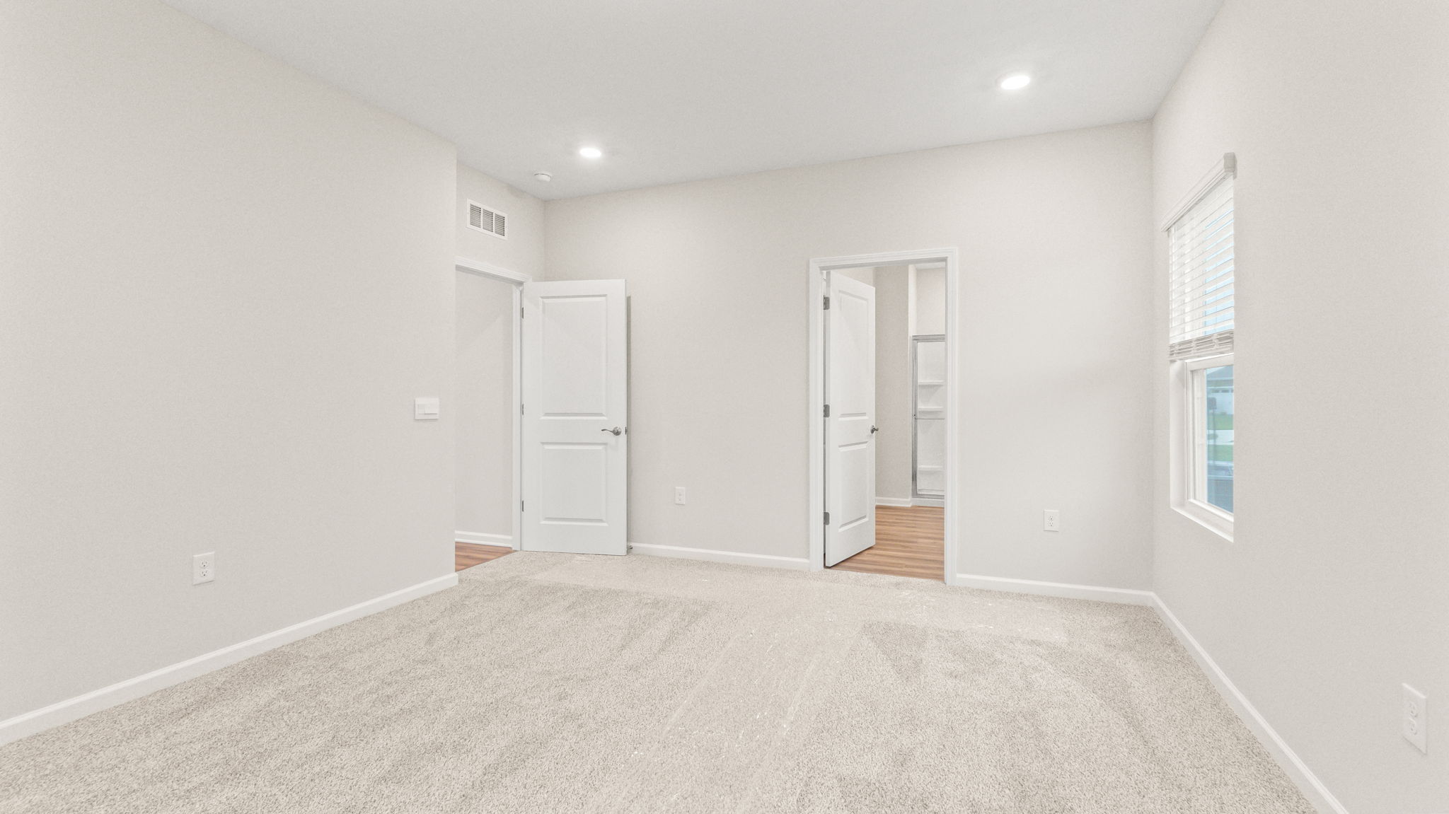 Carpeted primary bedroom with window and view of bathroom