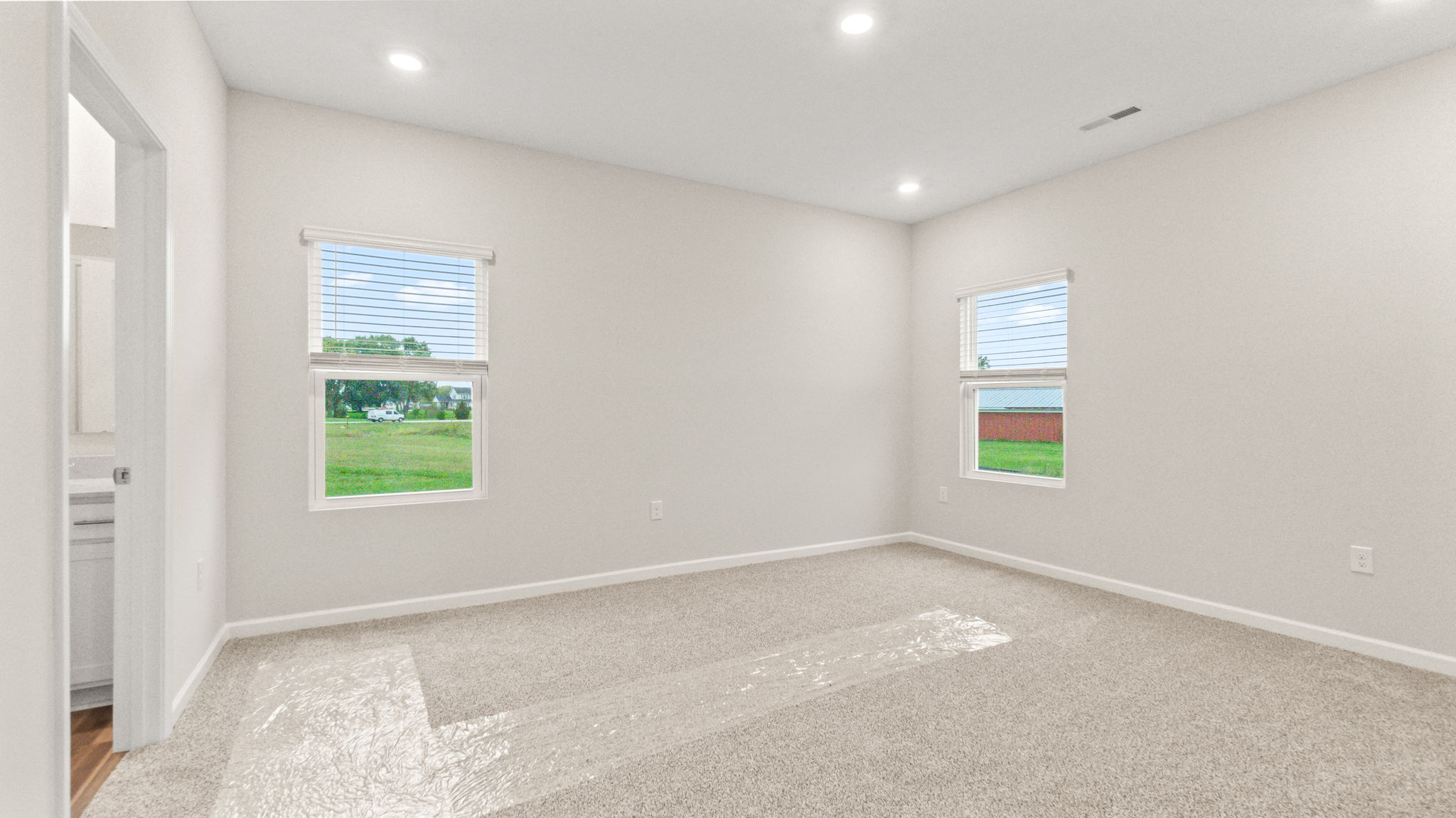 Carpeted primary bedroom with two windows and door to bathroom