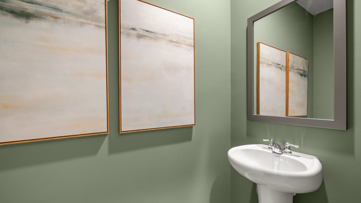Powder room with white sink, mirror, and two abstract art pieces on the green wall